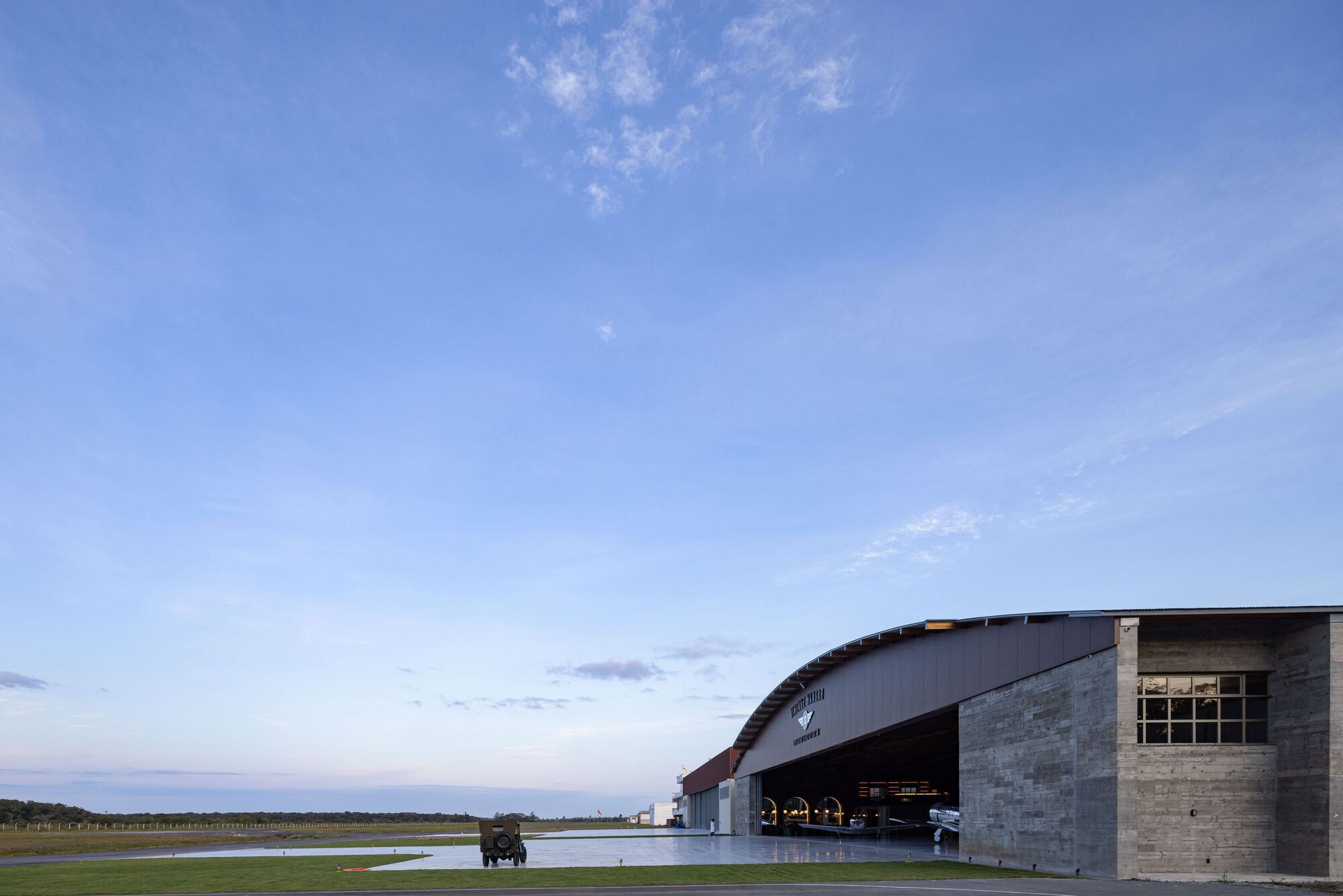 Exterior view of the curved metal hangar roof and concrete walls at dusk beside an airfield