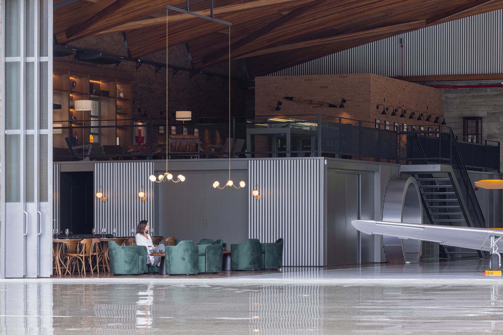 Mezzanine lounge area with corrugated metal partitions beneath the exposed timber ceiling and escalator beyond