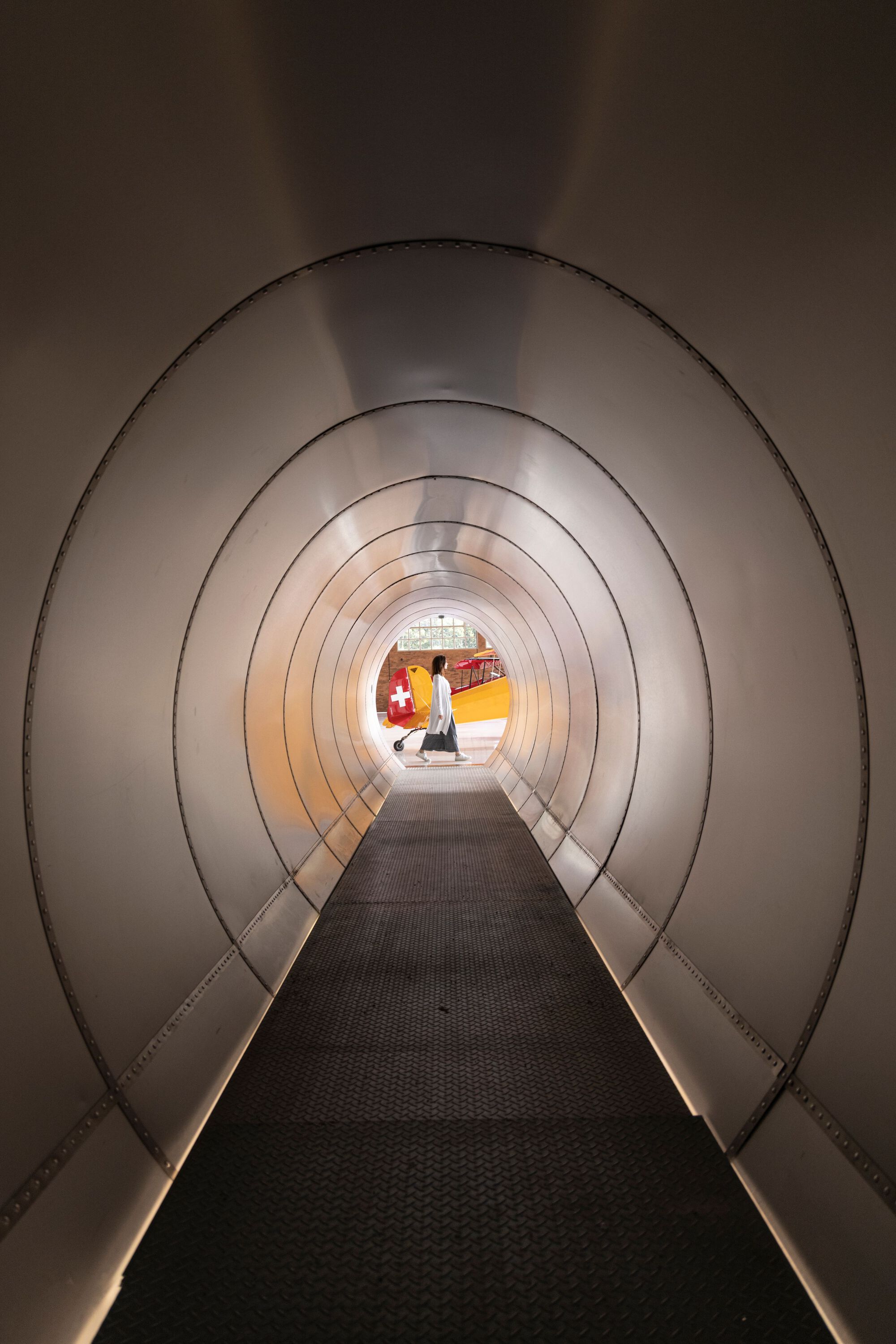 Curved tunnel corridor with ribbed metal walls and integrated strip lighting leading to the hangar floor