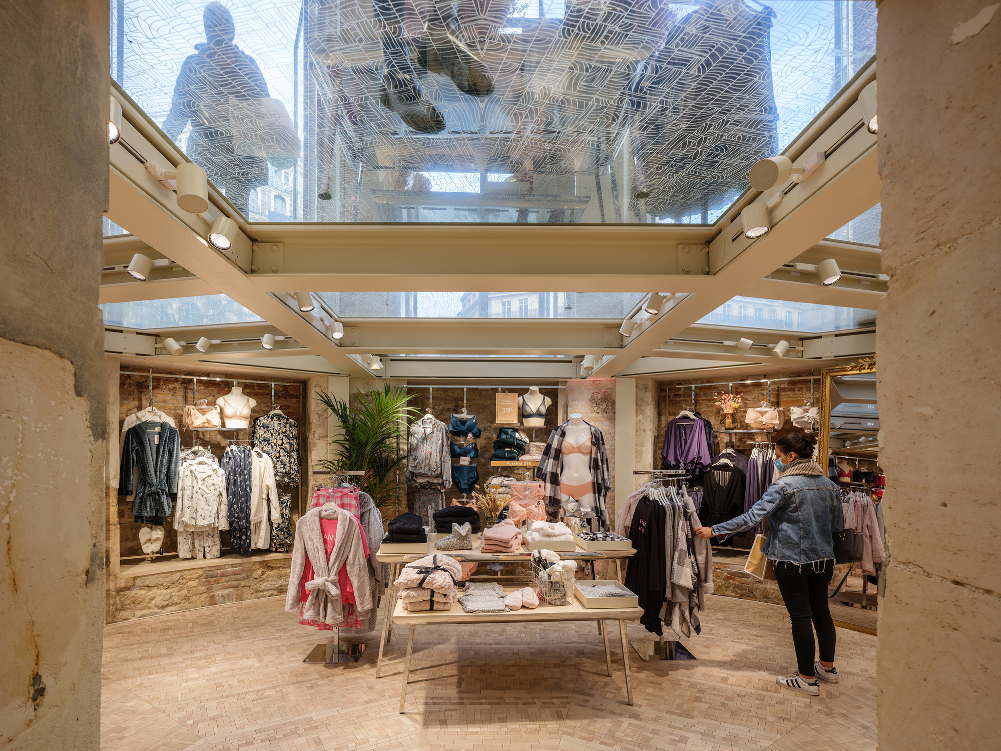 Retail interior with glass floor and skylight above showing shoppers browsing displays near limestone walls