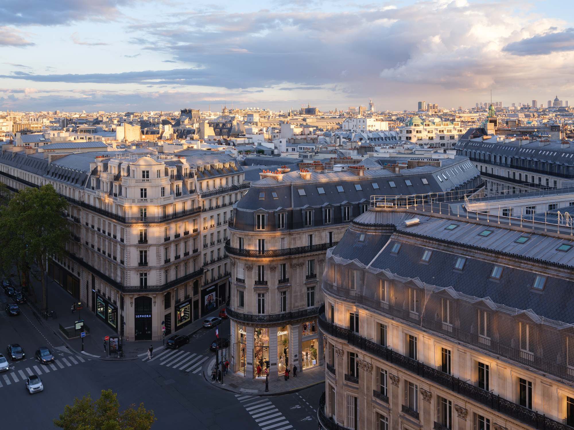 Aerial view of mansard rooftops and the curved corner building at street intersection during golden hour