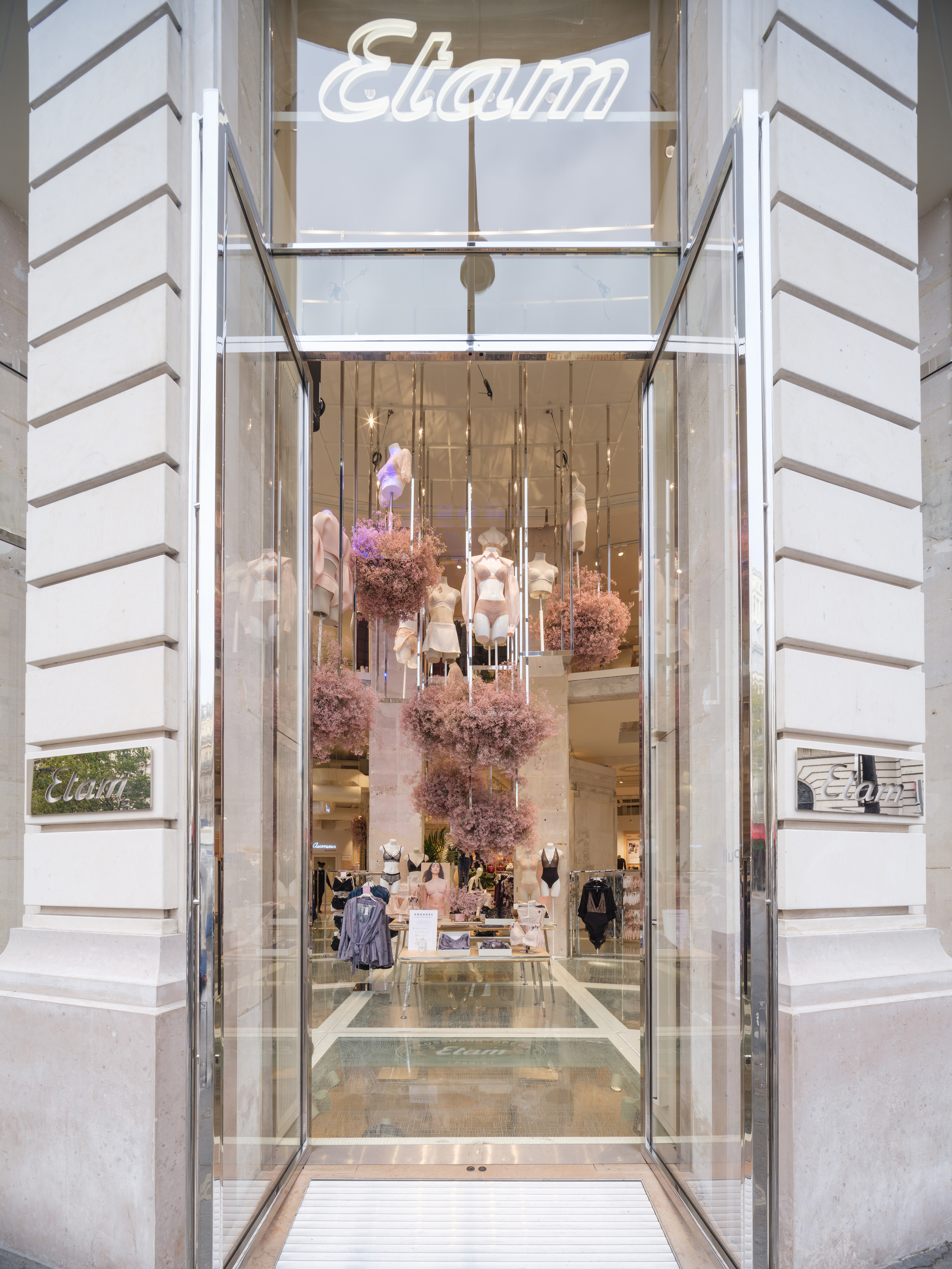 Entry threshold with glass doors and suspended floral installations visible through the transparent storefront