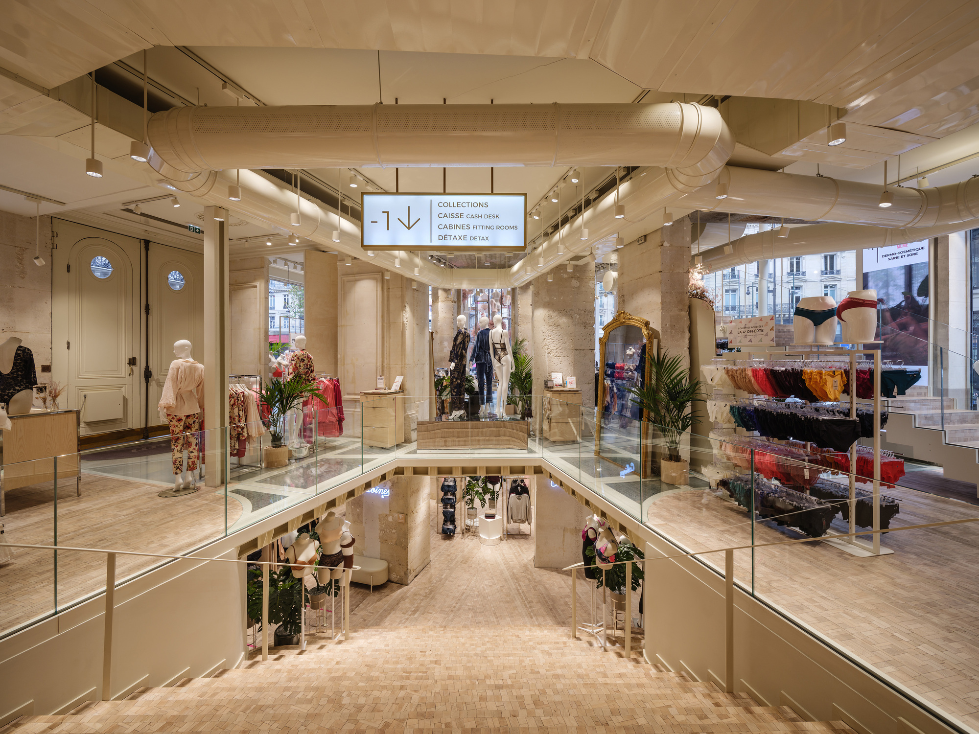 Upper level view of the retail floor with exposed ductwork and glass balustrade overlooking the lower level