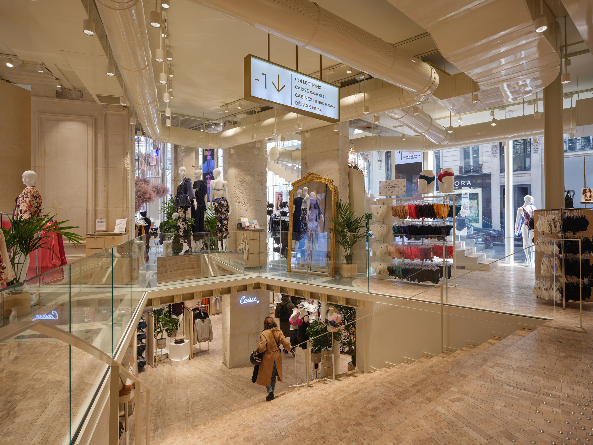 Glass-railed mezzanine surrounding the central atrium void with shoppers visible on the lower floor