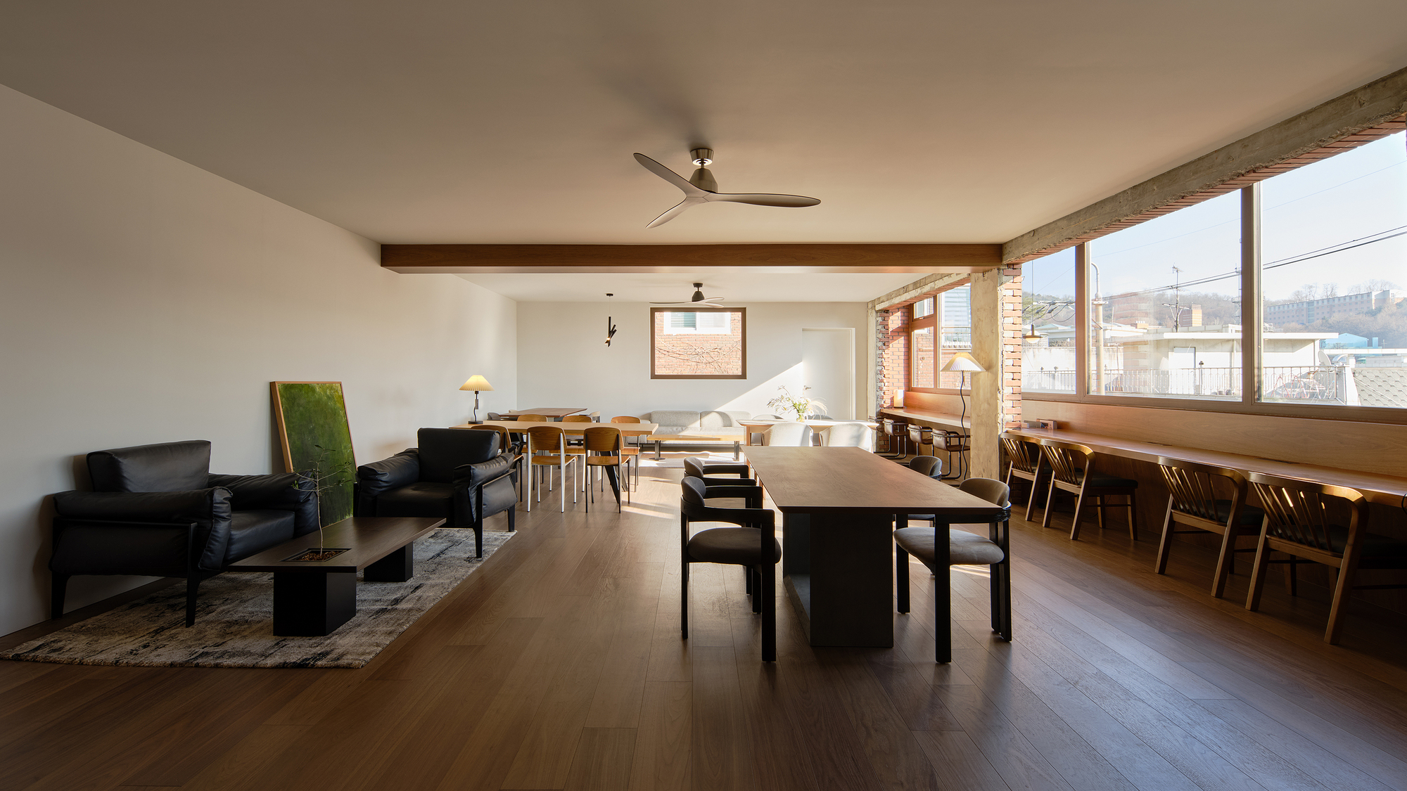 Open plan living and dining area with exposed brick wall and ribbon windows overlooking rooftops