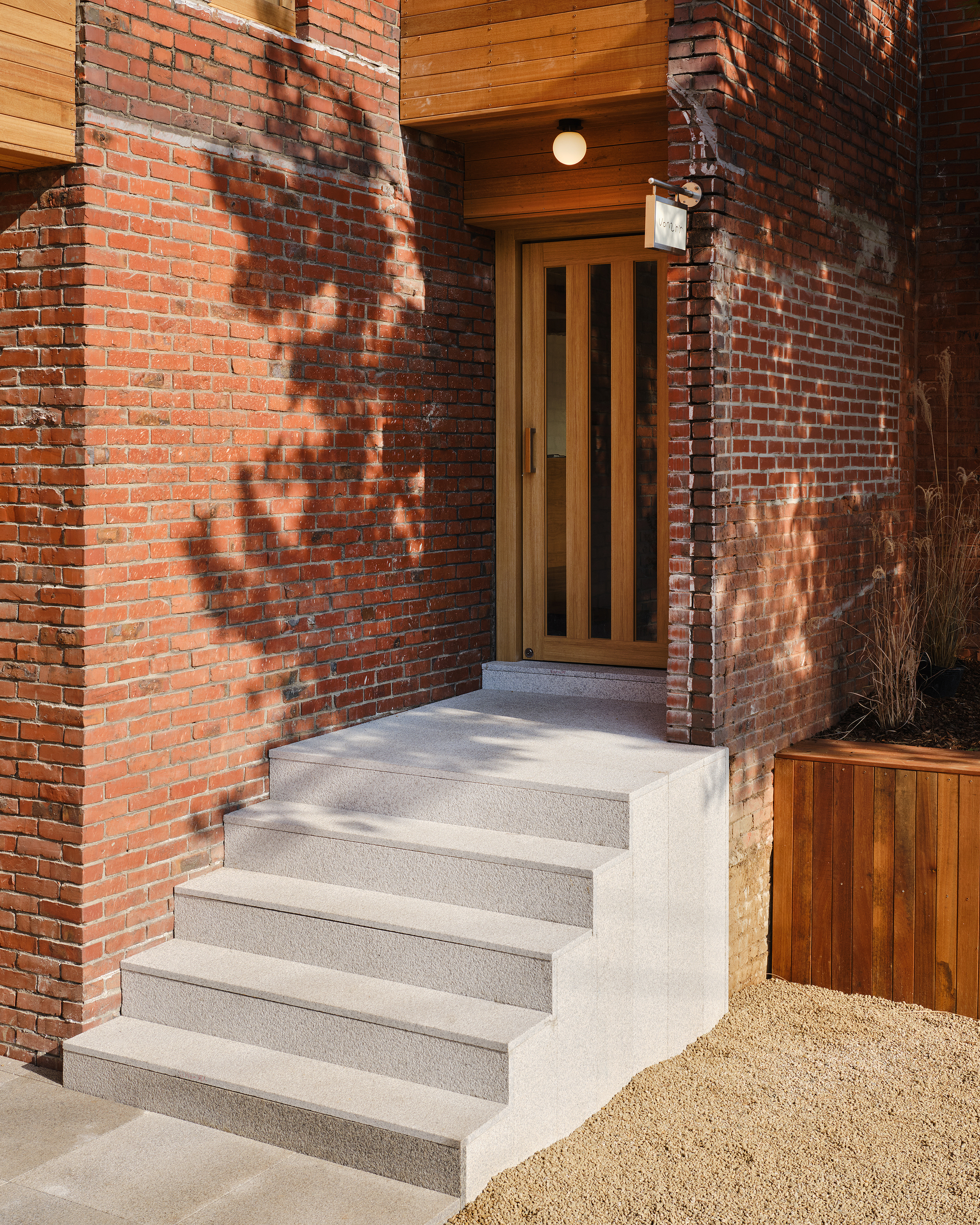 Exterior entry stair in poured concrete against weathered red brick wall in afternoon sunlight