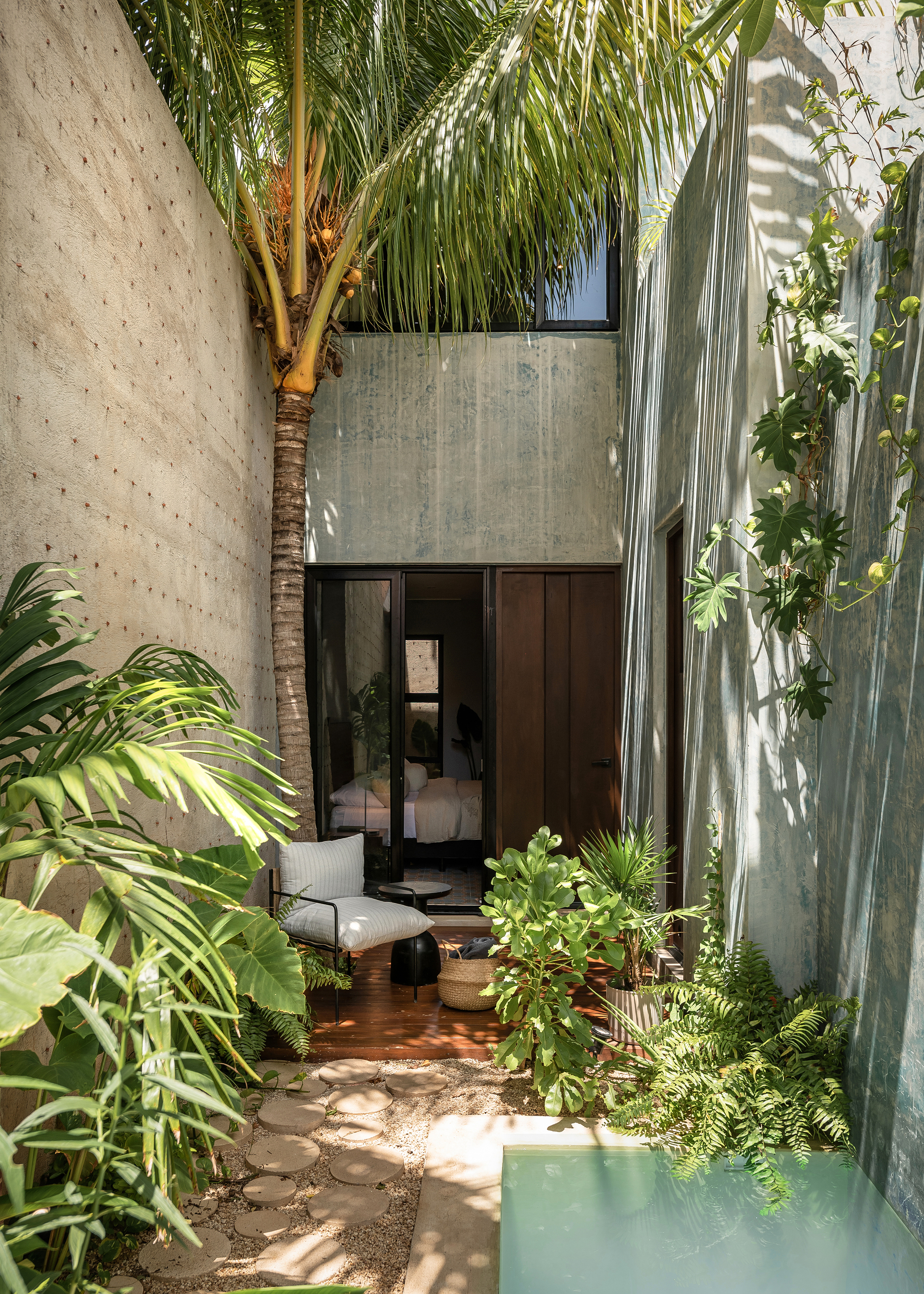 Narrow courtyard passage with stone pavers, planted beds, palm trunk and turquoise water channel