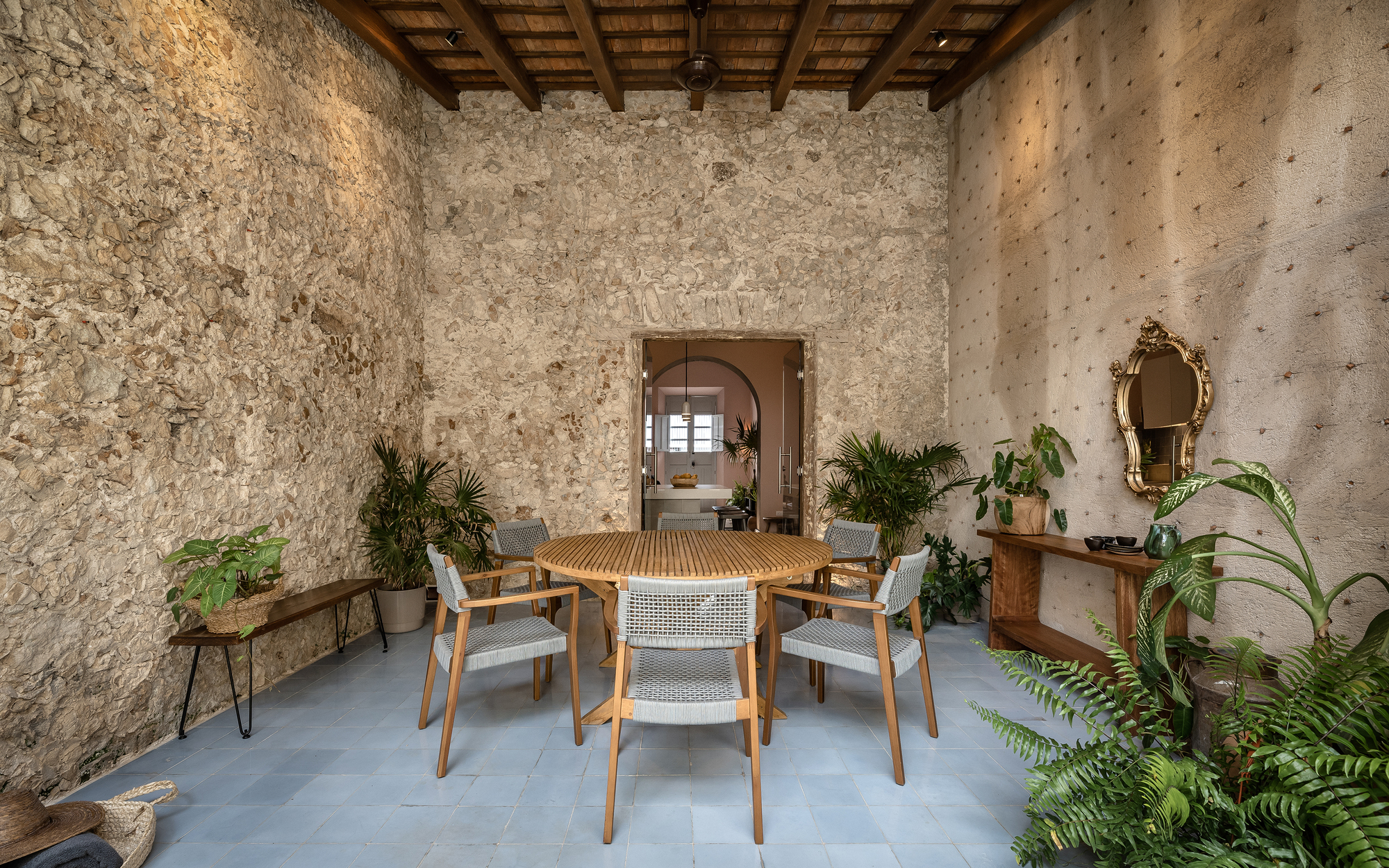 Dining room with exposed stone walls, timber ceiling beams, and polished concrete floor with potted plants