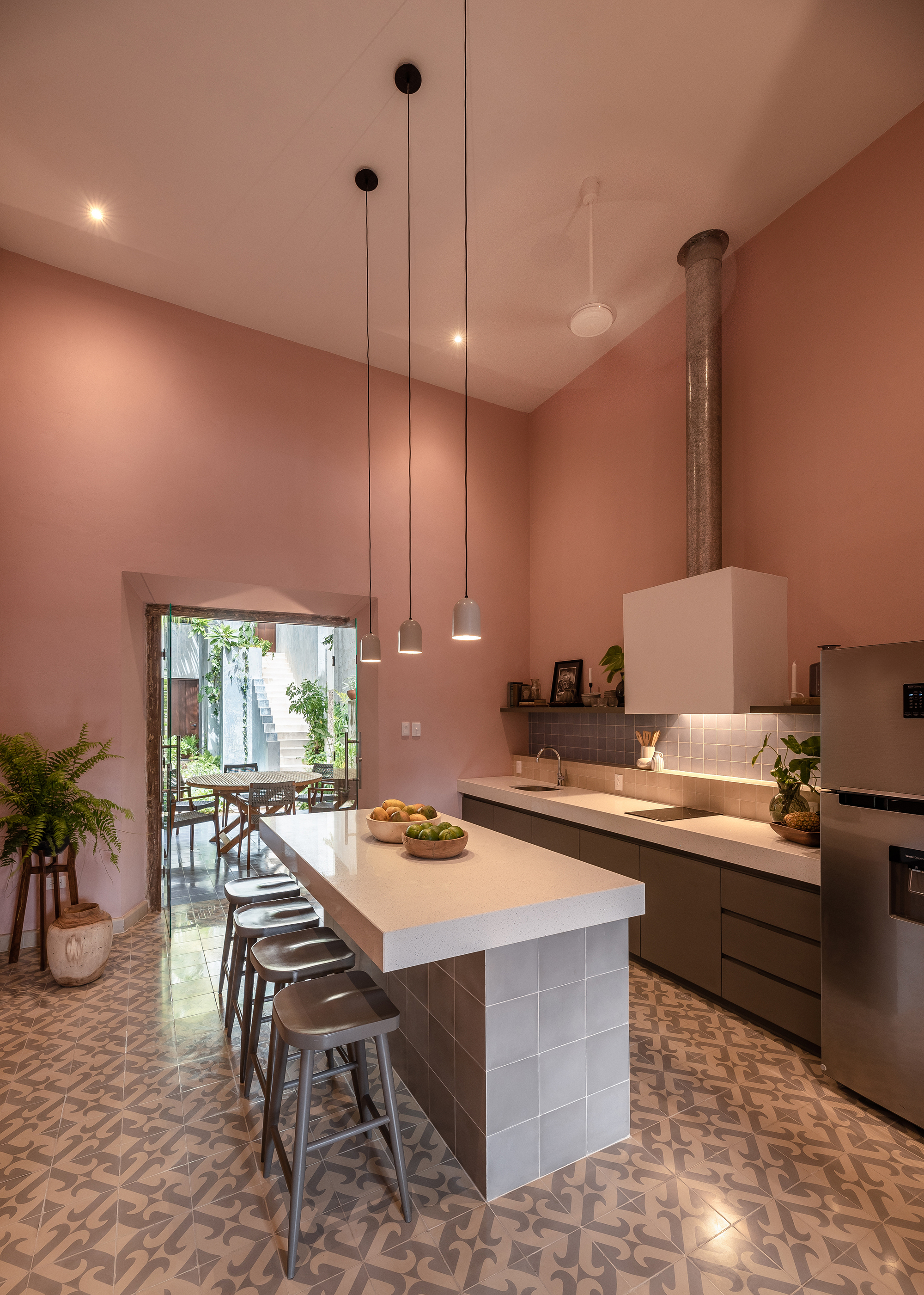 Kitchen with white-tiled island and pink plastered walls opening to a planted courtyard through an arched doorway
