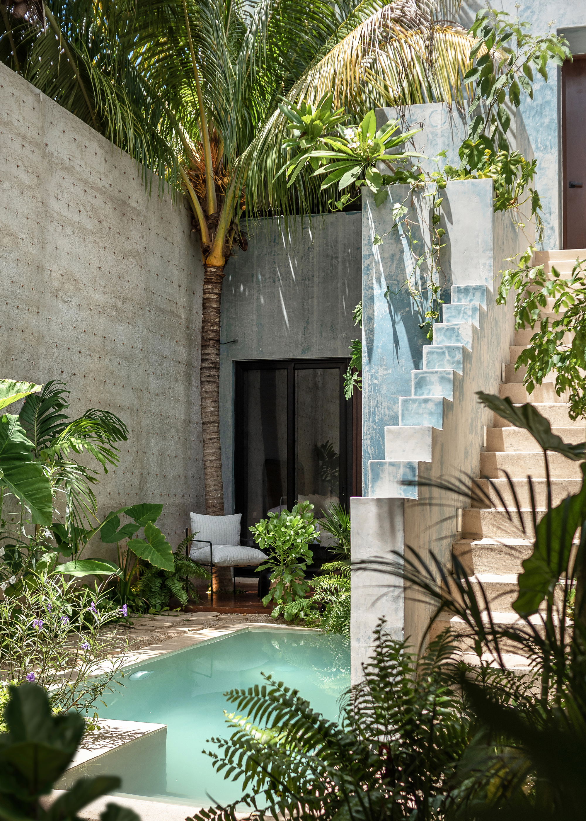 Interior courtyard with stepped staircase in weathered blue plaster and small pool surrounded by tropical plantings