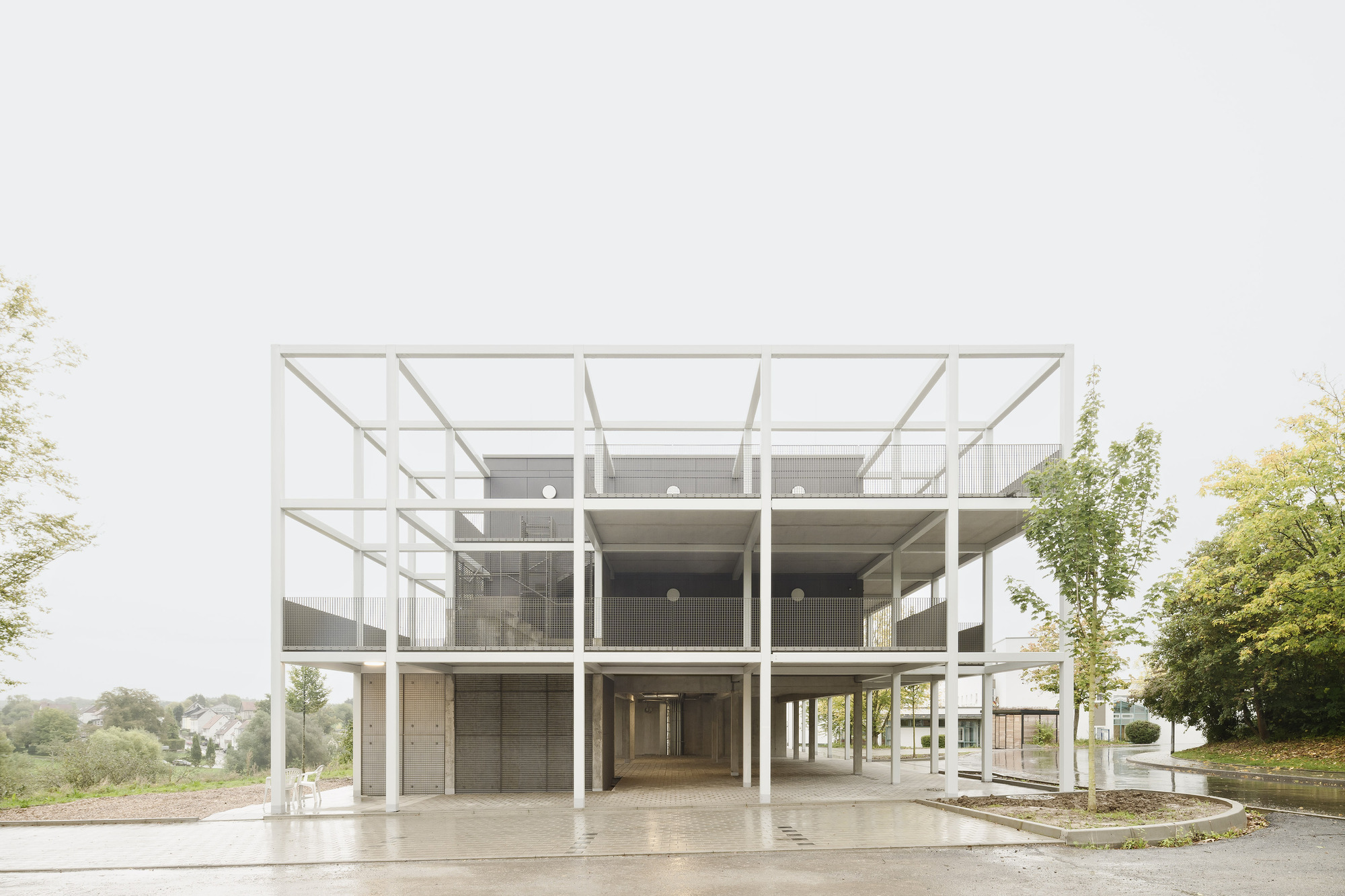 Three-storey white steel frame structure with glass infill and exposed columns on an overcast day
