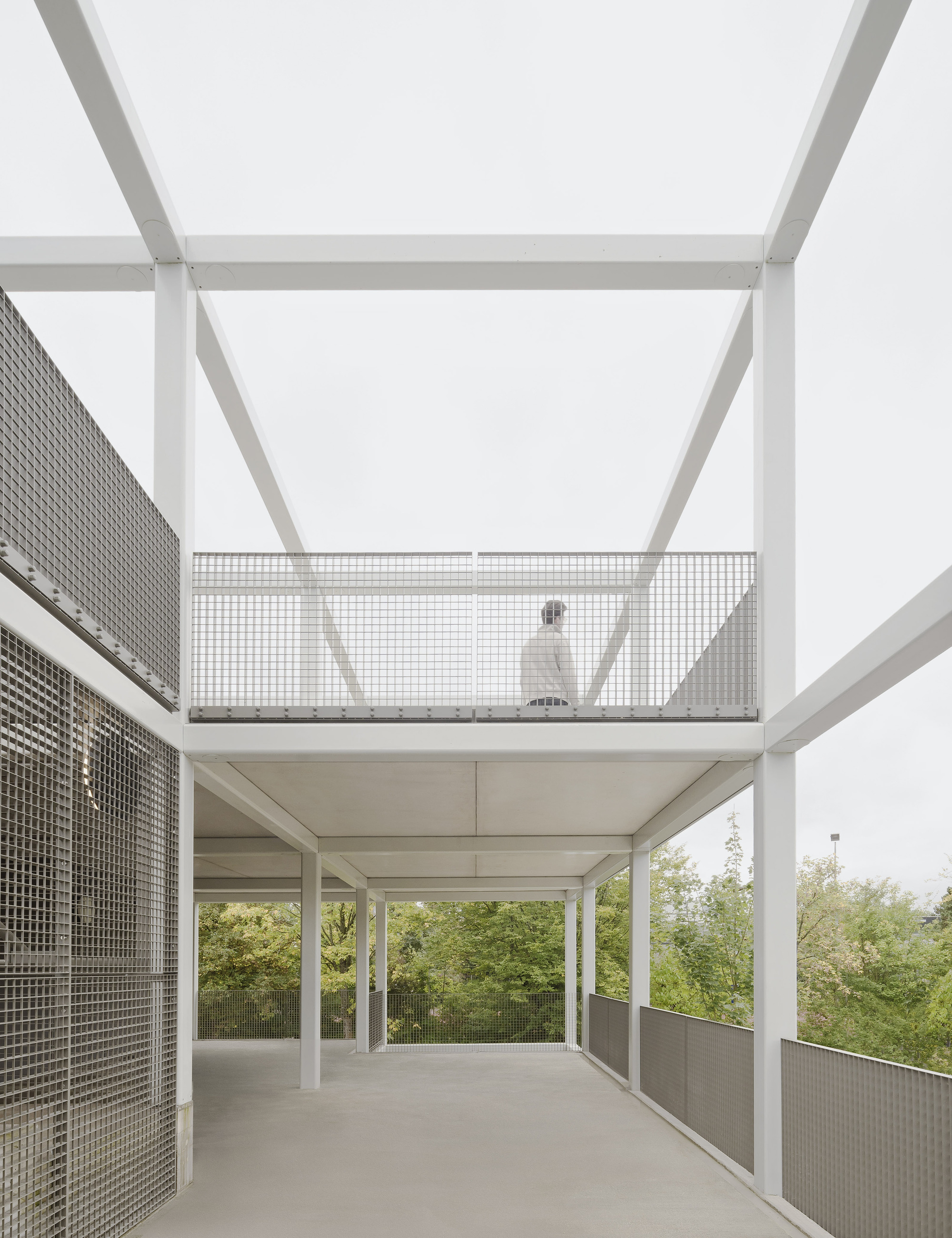 Open terrace with white steel structure and perforated metal balustrade with a figure walking on the upper level
