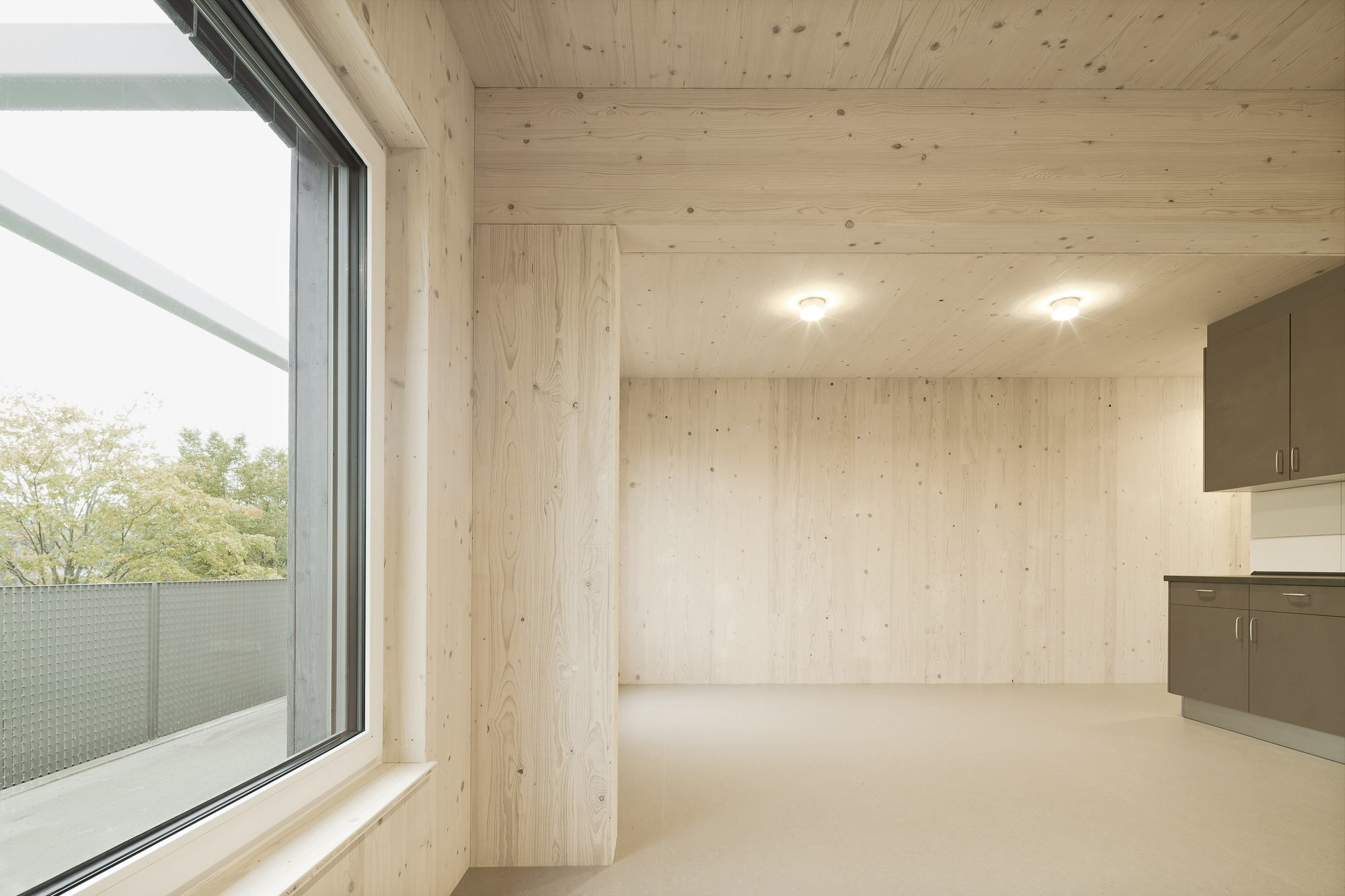 Interior room with exposed light timber plank walls and ceiling, cream flooring and a built-in grey kitchenette