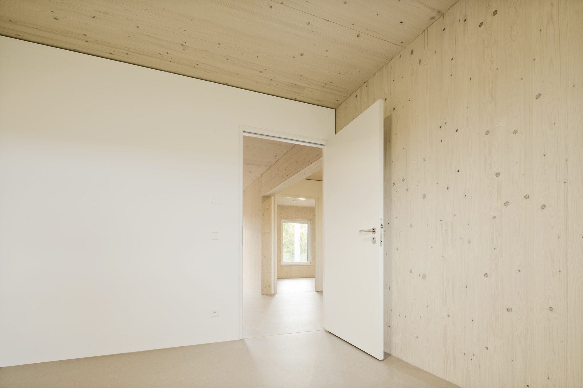 Doorway view through aligned rooms with exposed timber plank walls and white painted partitions under natural light