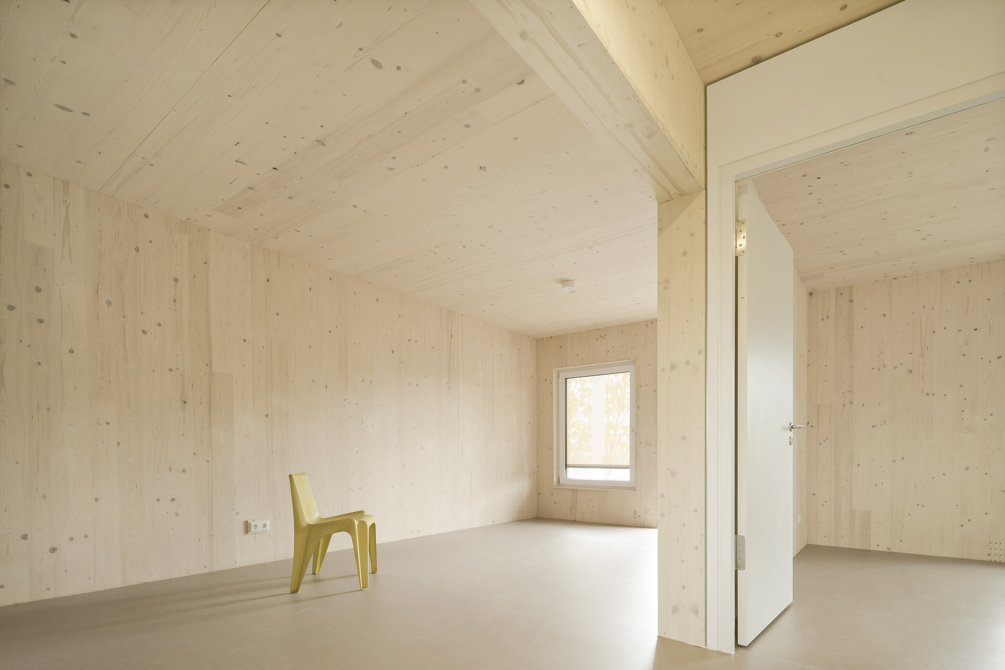 Interior room with light plywood walls and ceiling, pale resin flooring and a yellow plastic chair