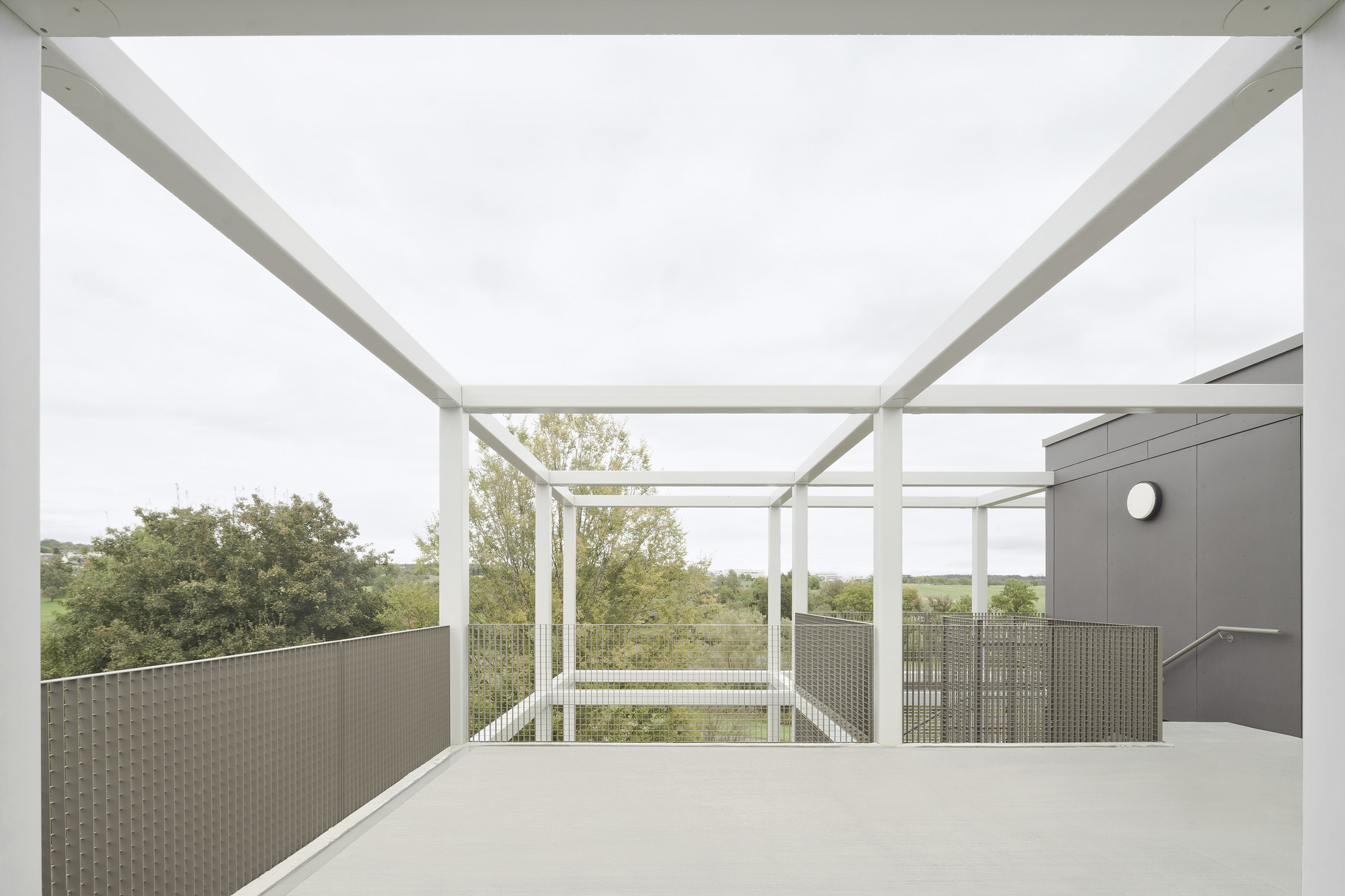 Open-air terrace with white structural frame, mesh balustrades and views to distant green countryside