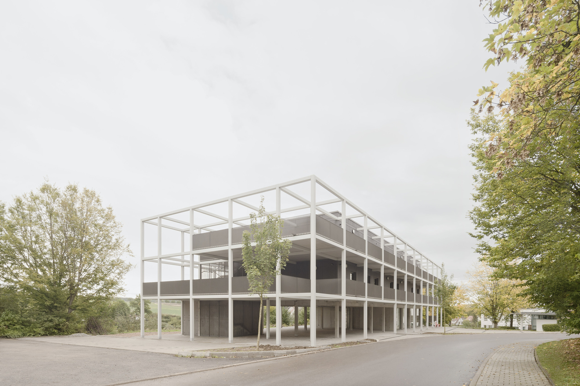 Corner view of the white steel frame structure with infill panels among deciduous trees