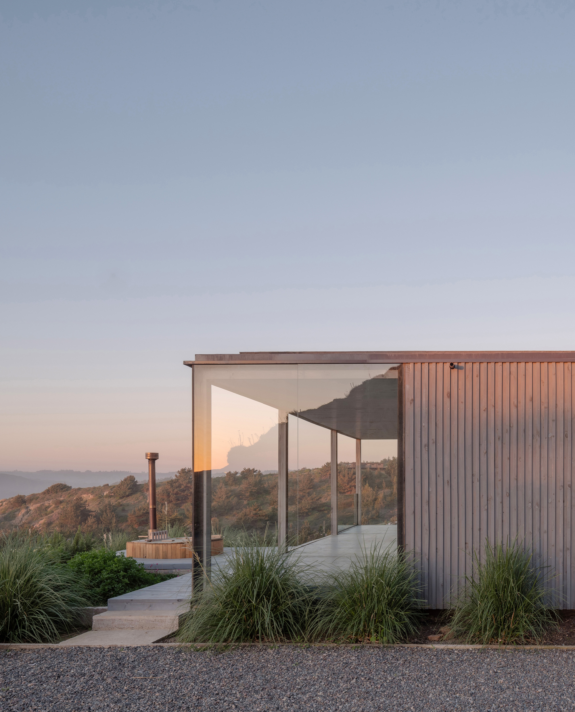Curved concrete pathway leading to covered terrace with vertical timber cladding and ornamental grasses at sunset