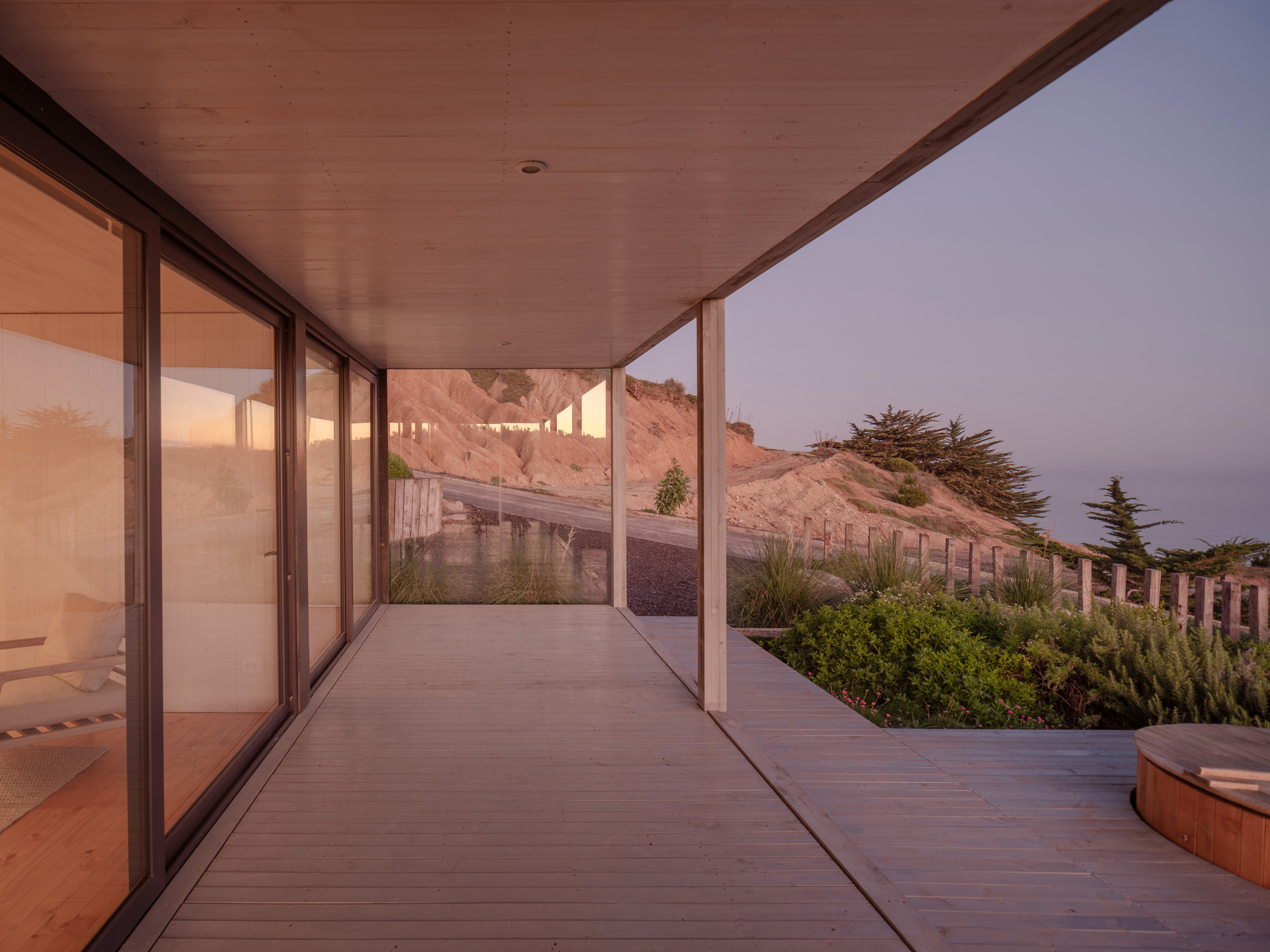 Covered timber deck with sliding glass walls overlooking terraced hillside and planted beds at dusk