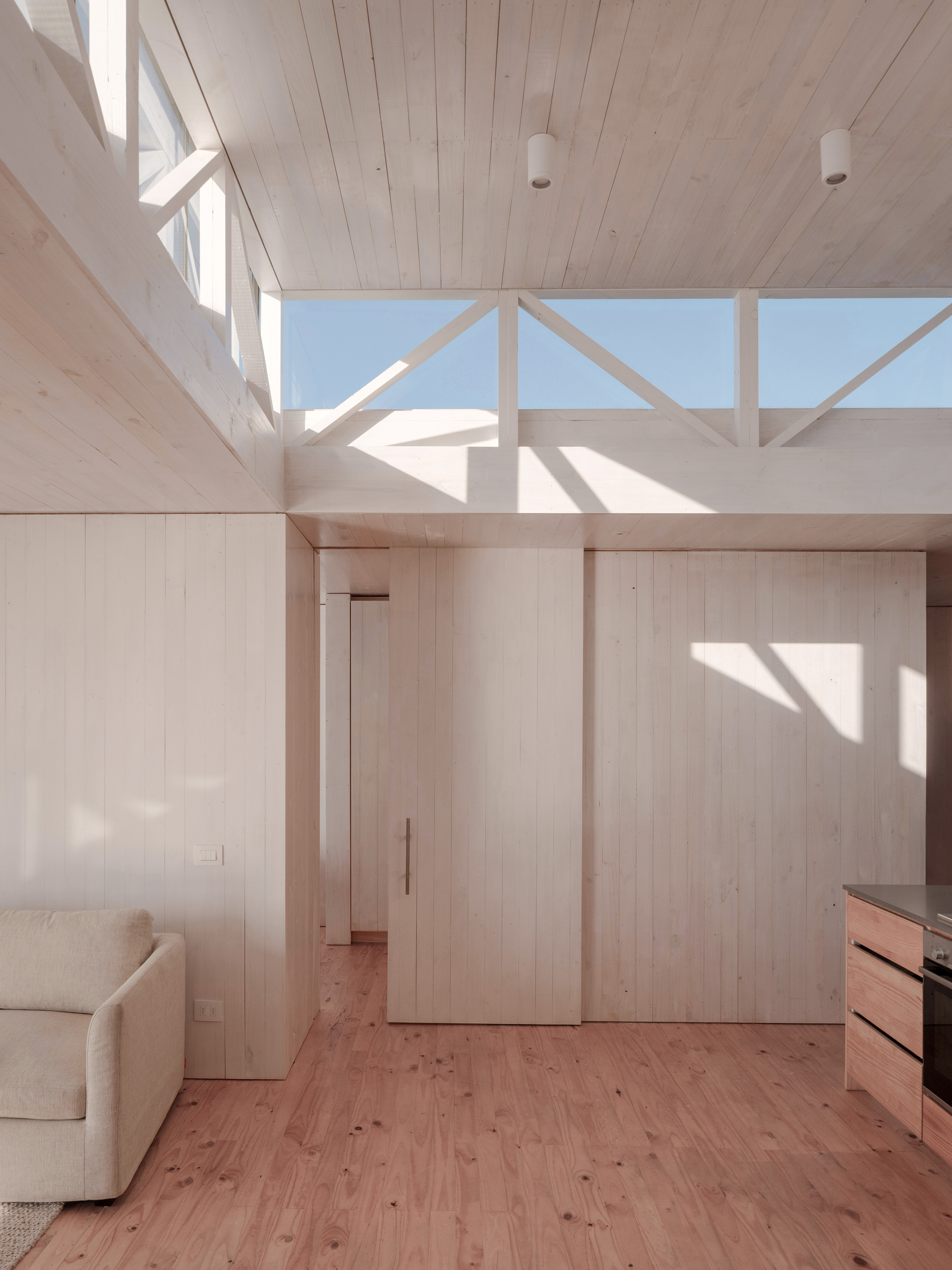 Light-filled interior with pale timber walls, exposed ceiling beams, and clerestory windows casting shadows across the floor