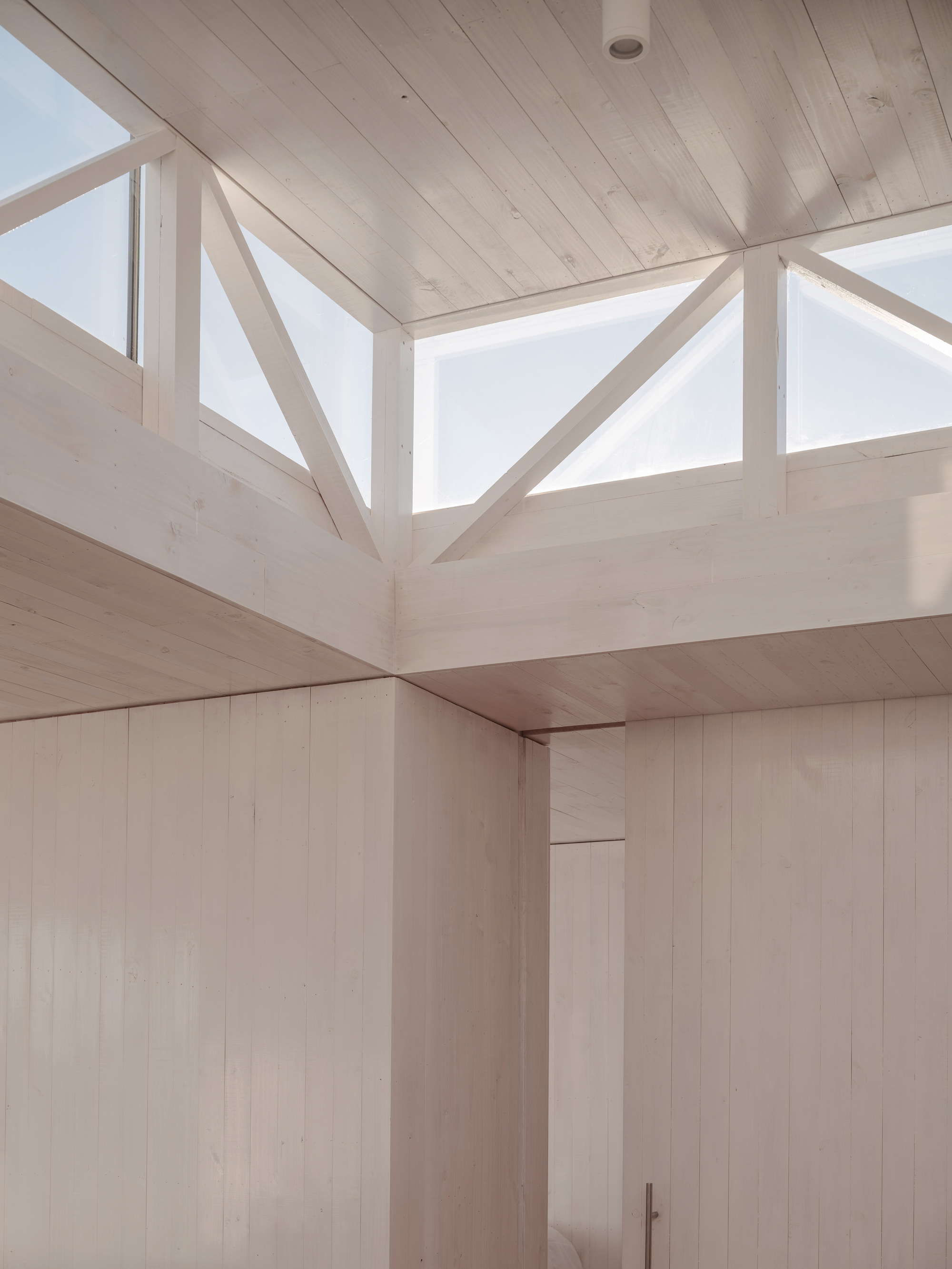 Upward view of the timber-framed clerestory window assembly with triangular bracing under a pale wood ceiling