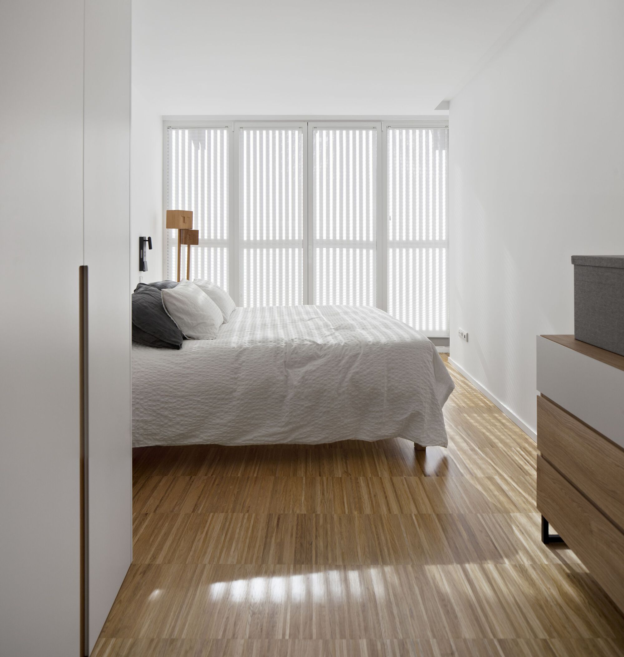 Bedroom view through a timber-framed doorway with vertical blinds casting striped shadows on the floor