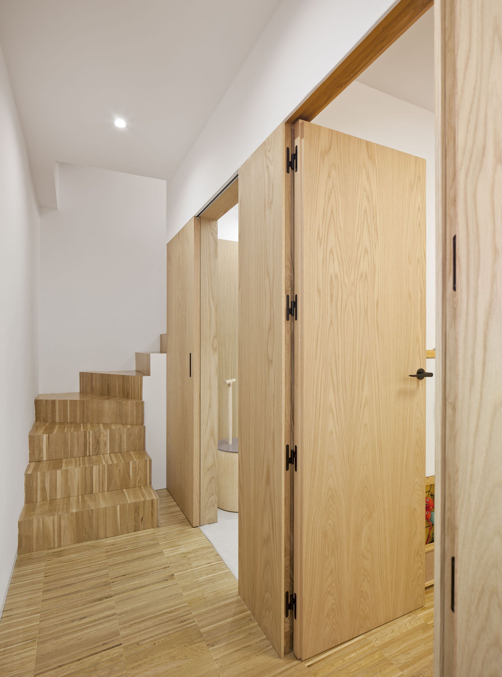 Light oak staircase and flush door beneath a sloped ceiling in a narrow corridor