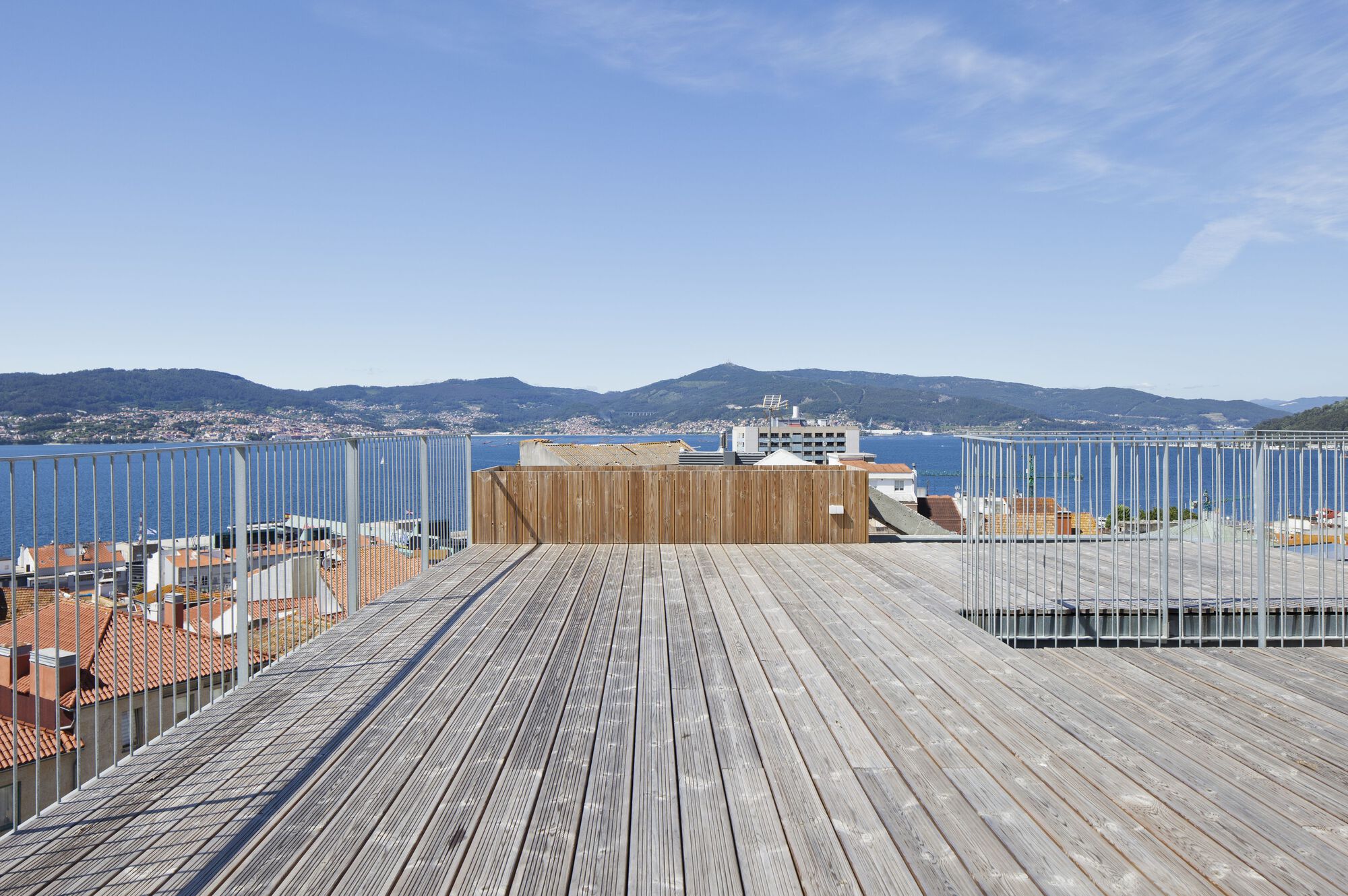Rooftop timber deck with vertical slat railing overlooking a bay and distant hills