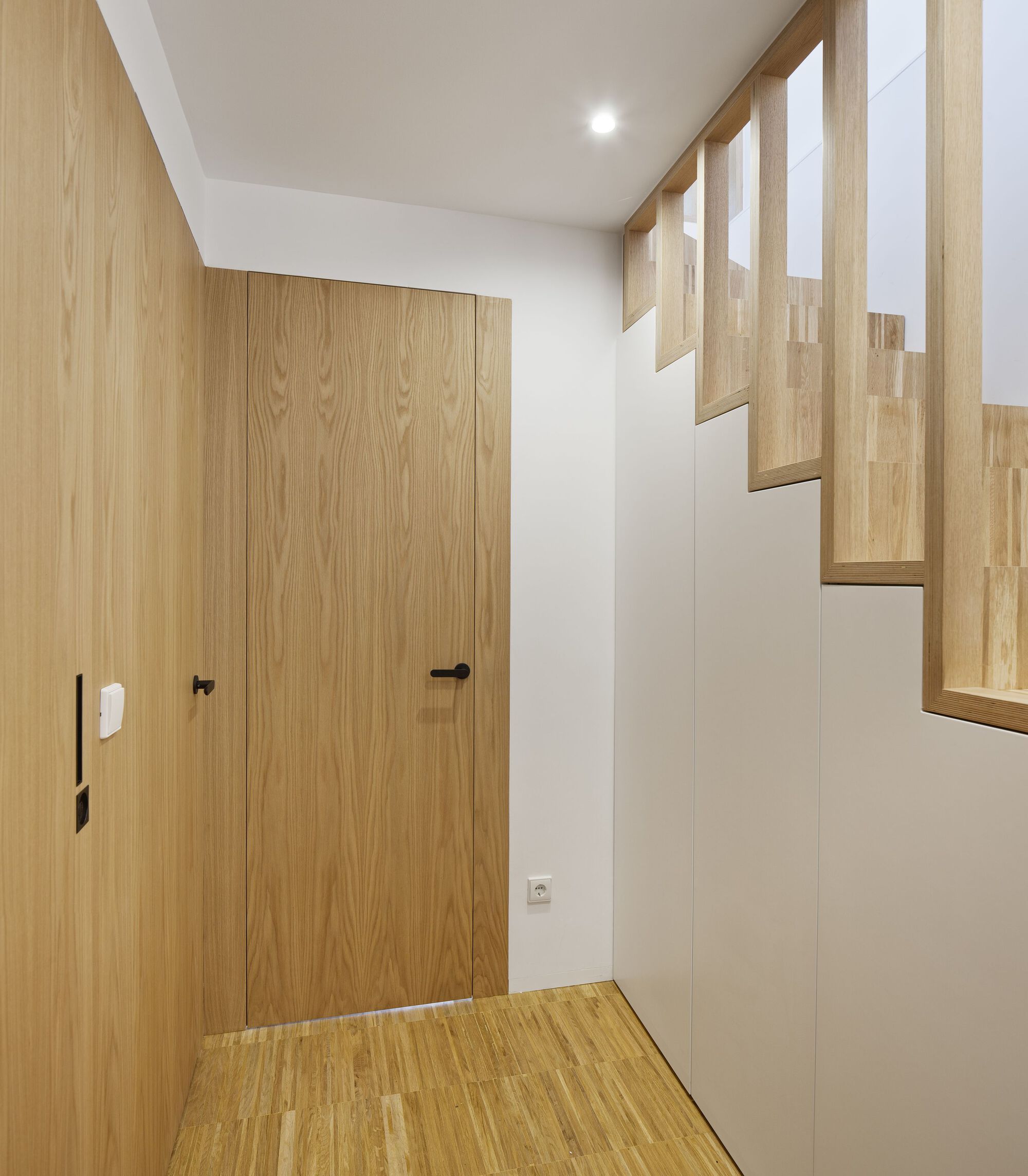 Entry vestibule with oak-clad door and open-tread staircase ascending along the wall