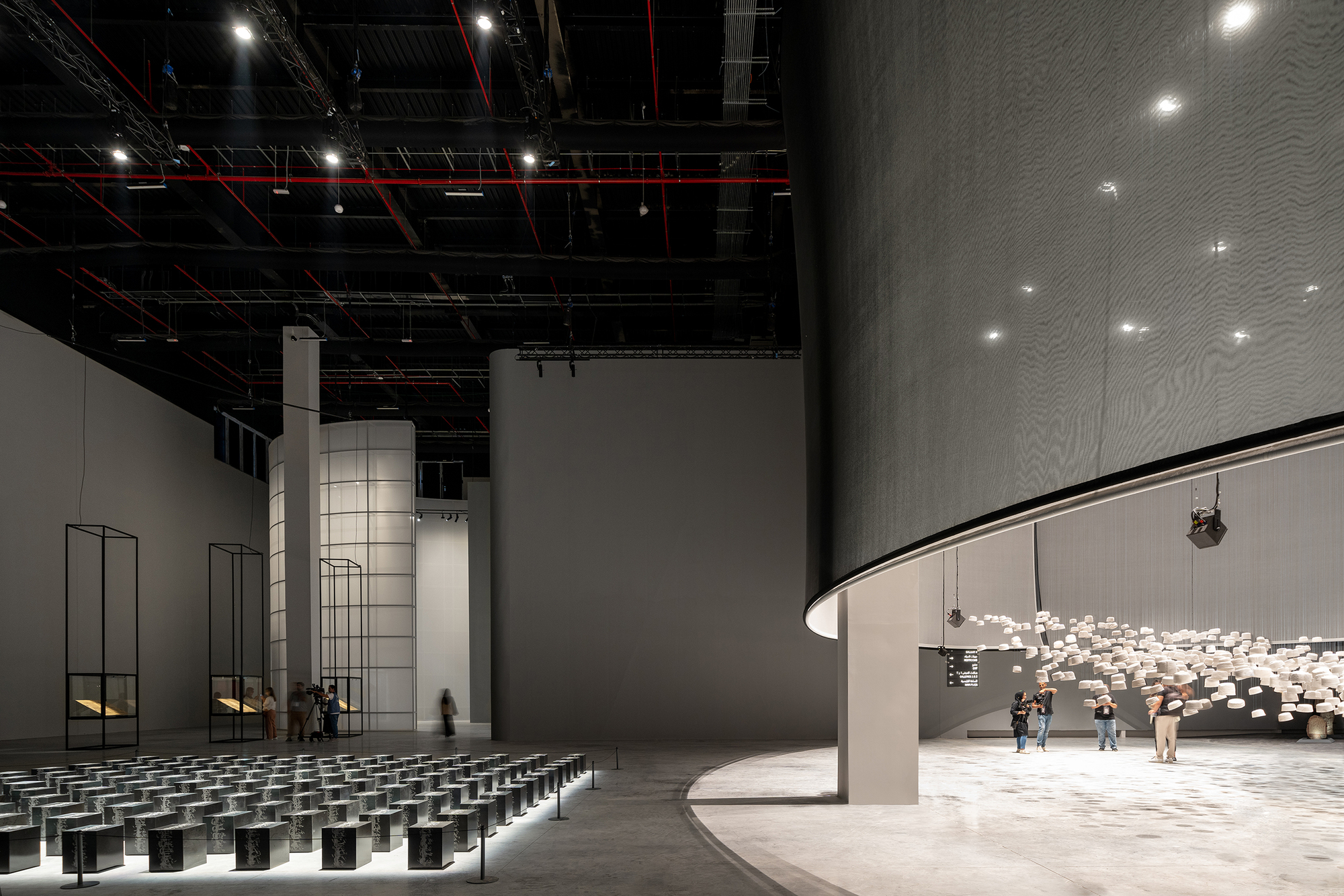 Interior auditorium with curved balcony, exposed black ceiling infrastructure, and rows of dark seating cubes