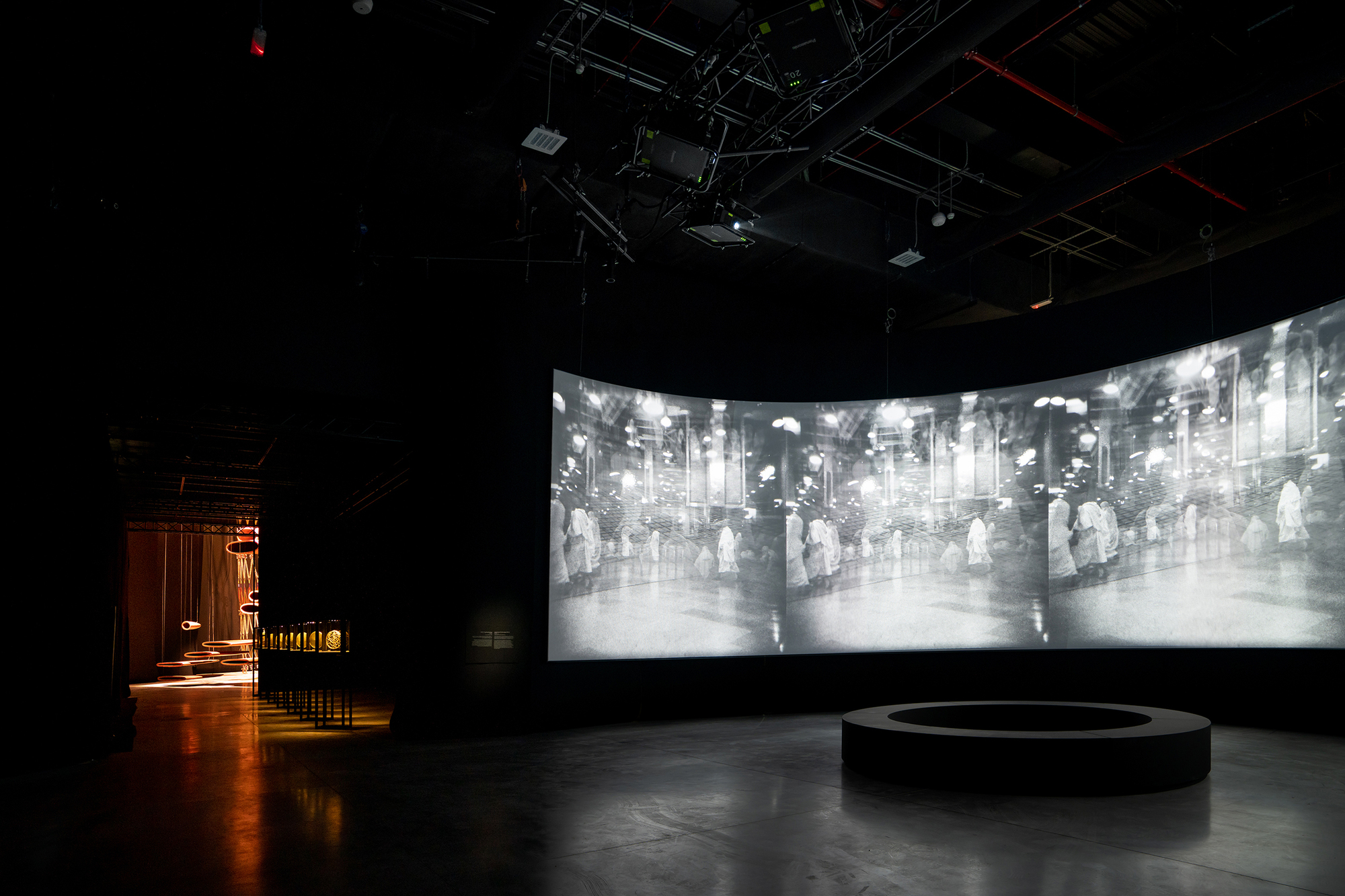 Curved projection screen displaying archival imagery above a circular platform in a darkened exhibition space