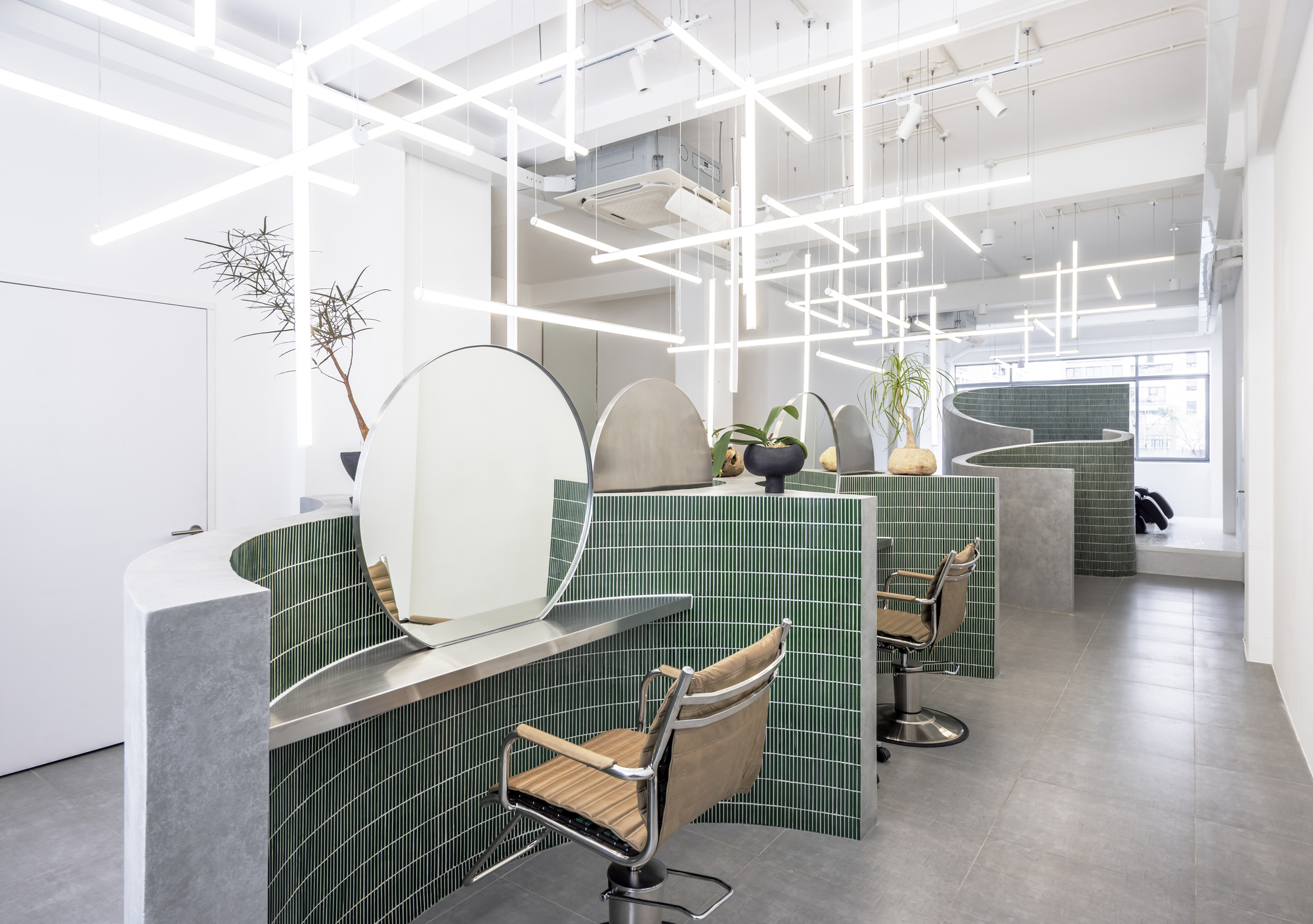 Salon interior with green mosaic tile partitions and arched mirrors beneath a white linear lighting grid