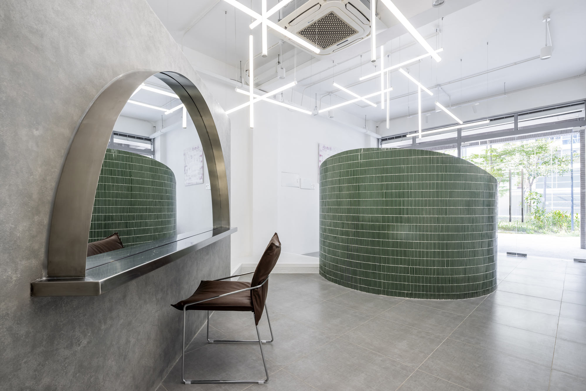 Curved green tile wall with arched concrete canopy and a wooden chair near daylit storefront windows