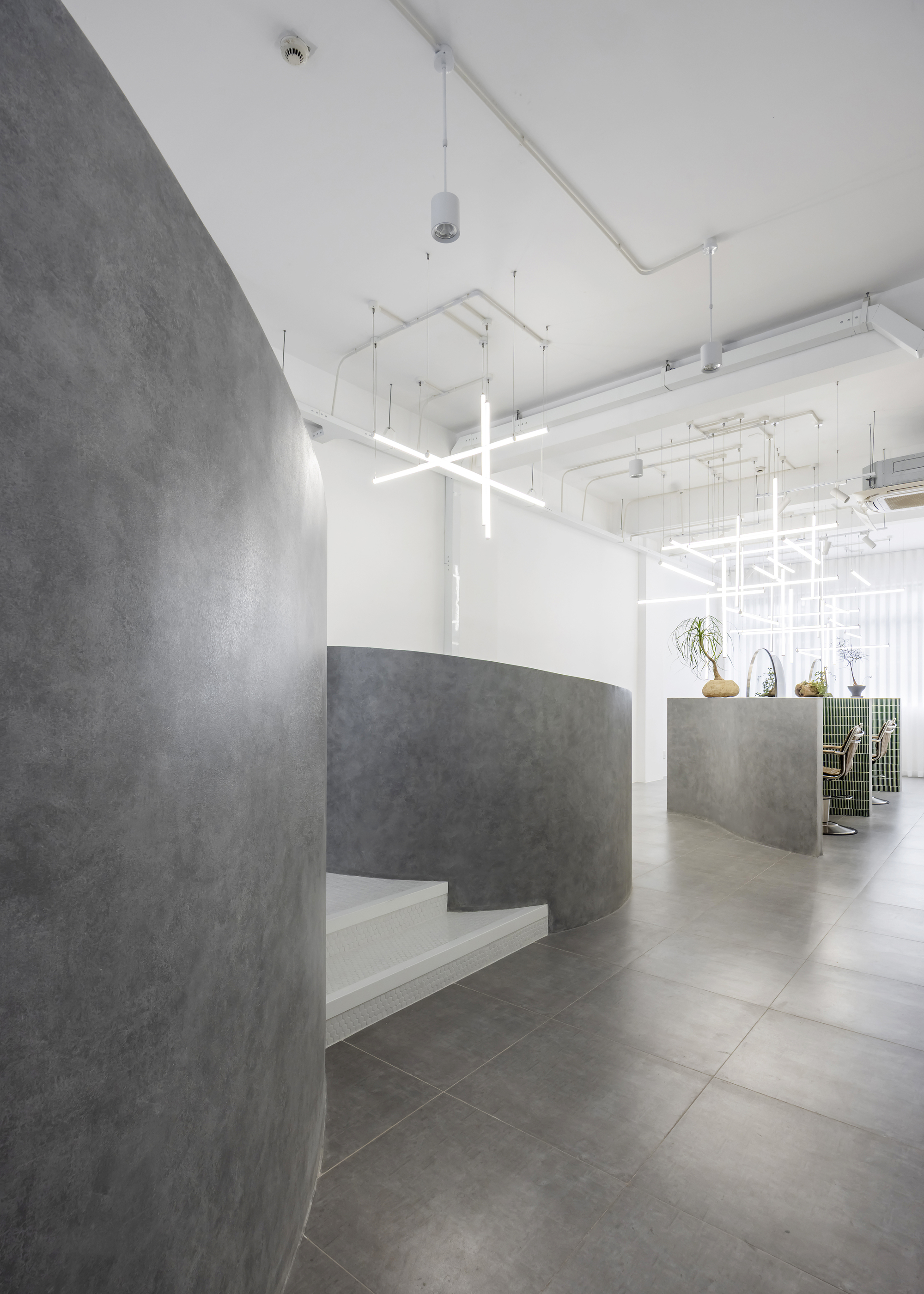 Curved concrete reception desk with built-in bench seating beneath exposed white ceiling and linear lighting