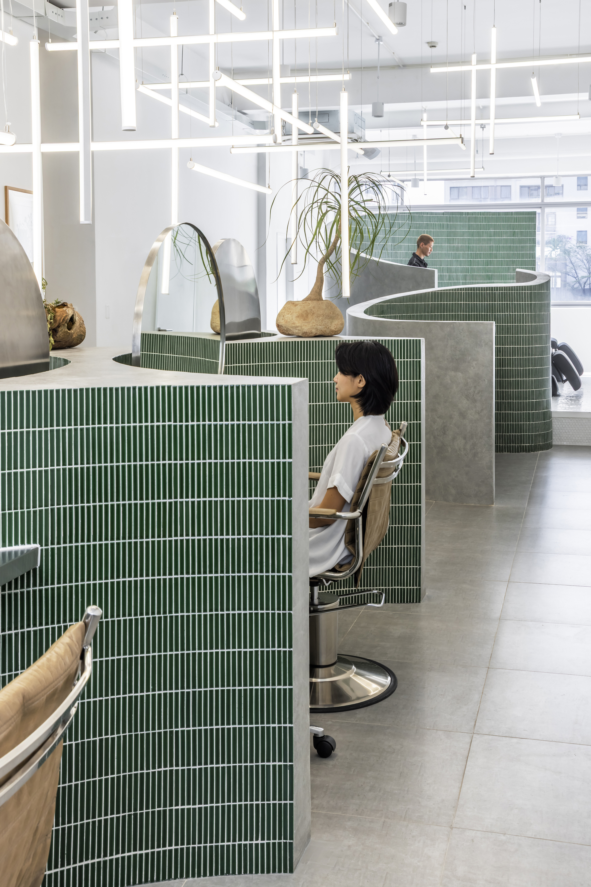 Green mosaic tile partition walls with curved concrete tops separating salon workstations