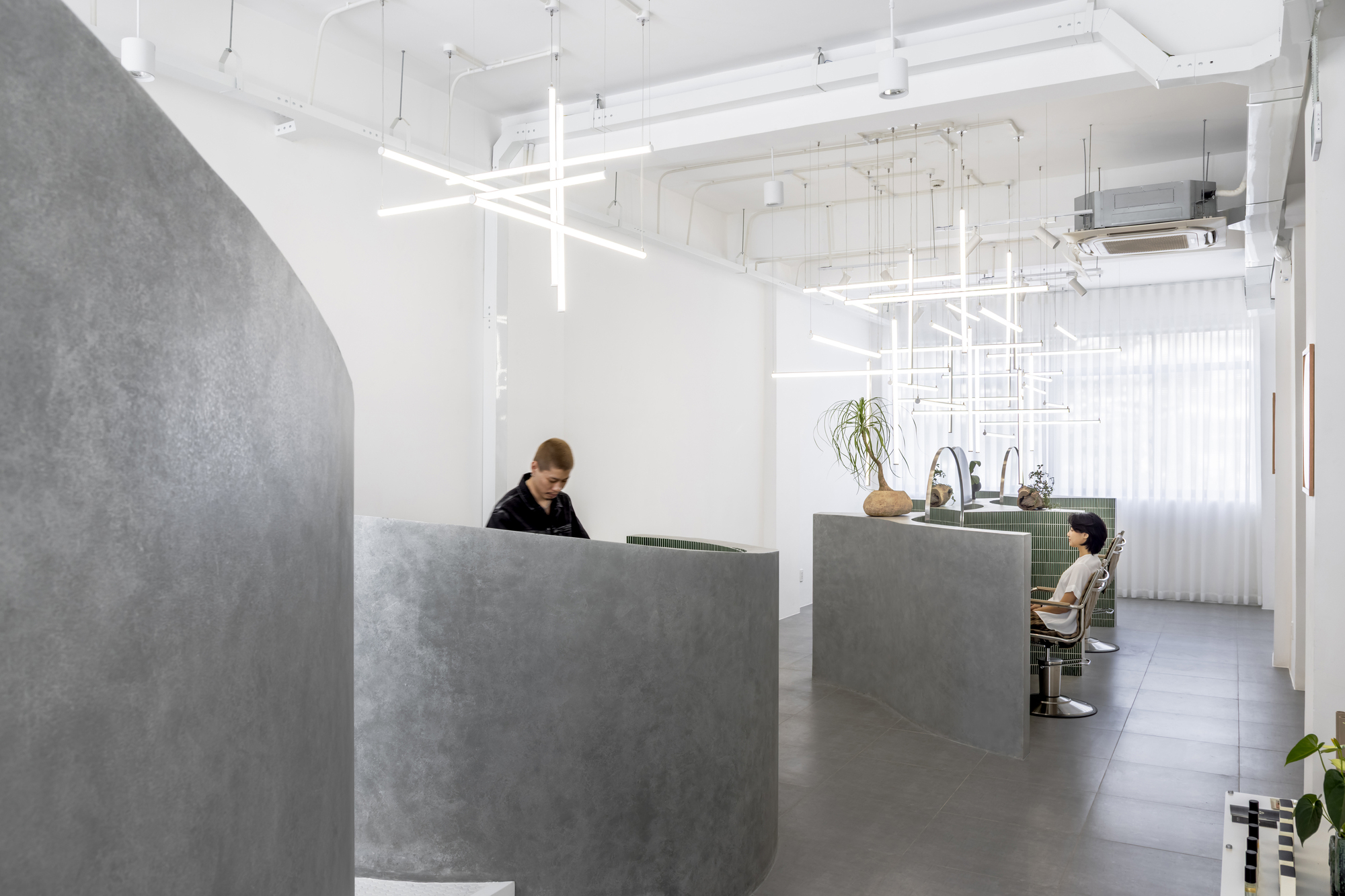 Reception area with curved concrete desk under suspended white linear lighting grid and sheer curtains
