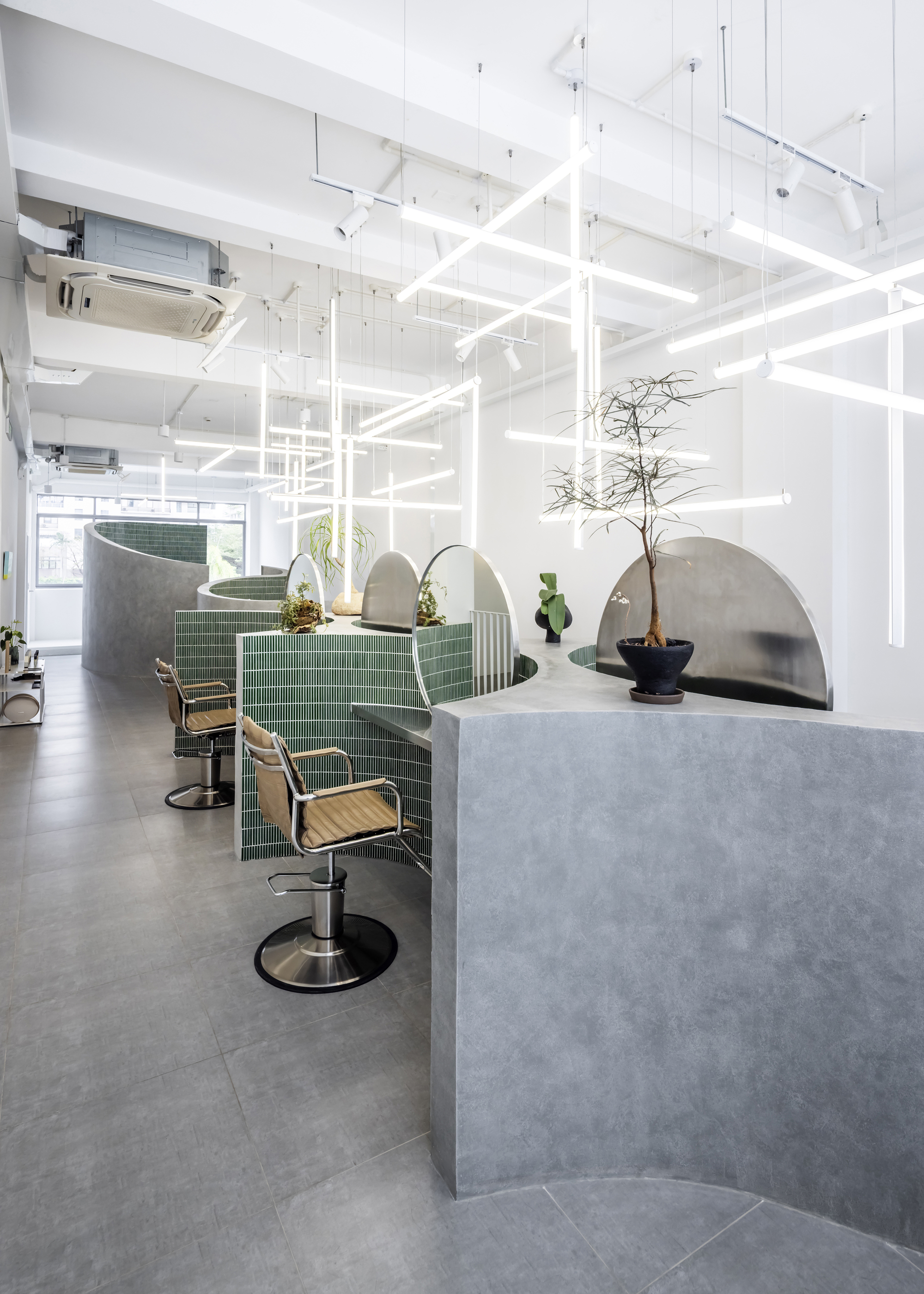 Salon workstations with green tile partitions, curved concrete screens and potted plants under grid lighting