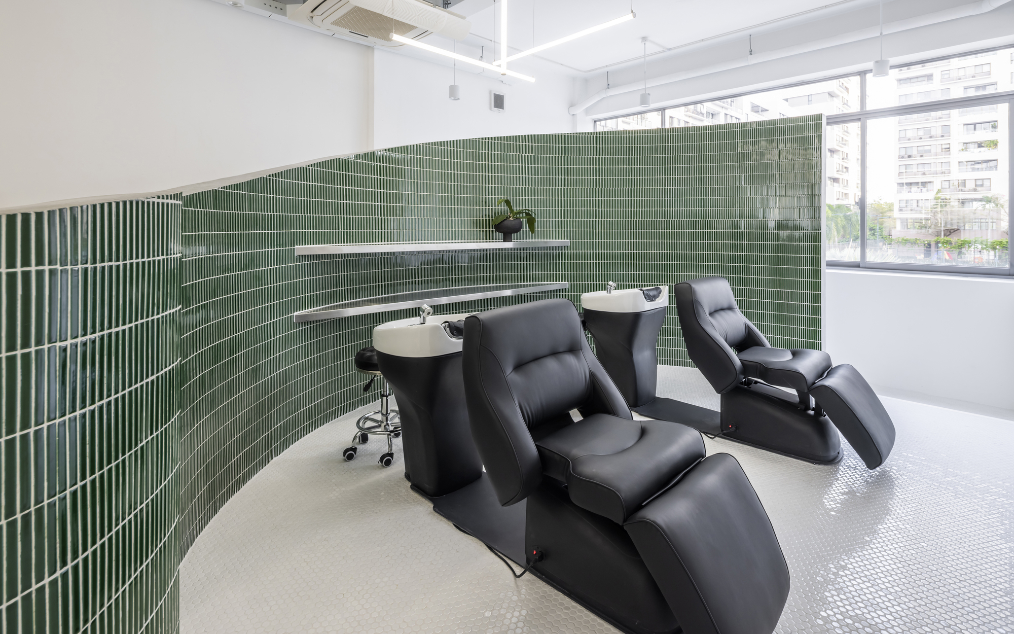 Hair washing area with reclined black chairs against curved green tile wall near windows