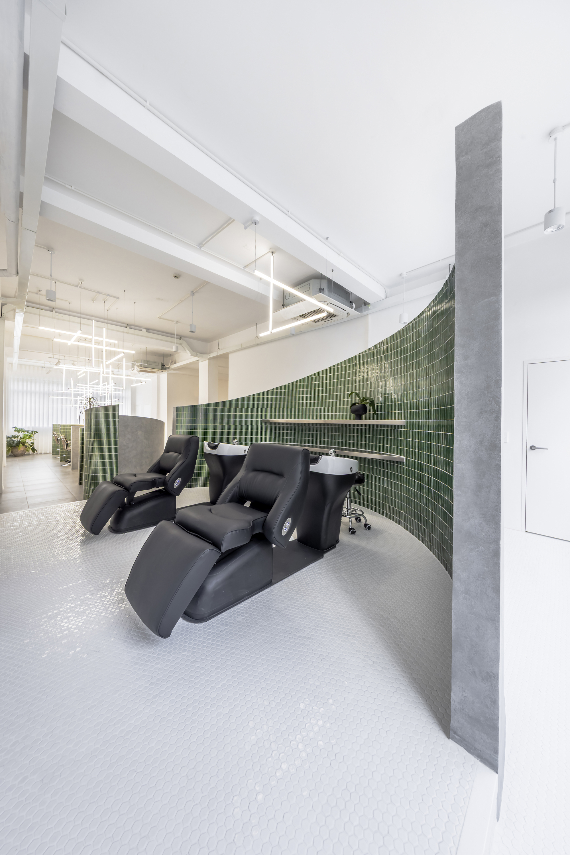 Salon interior with black reclining chairs against a curved green tile wall beneath exposed ceiling beams