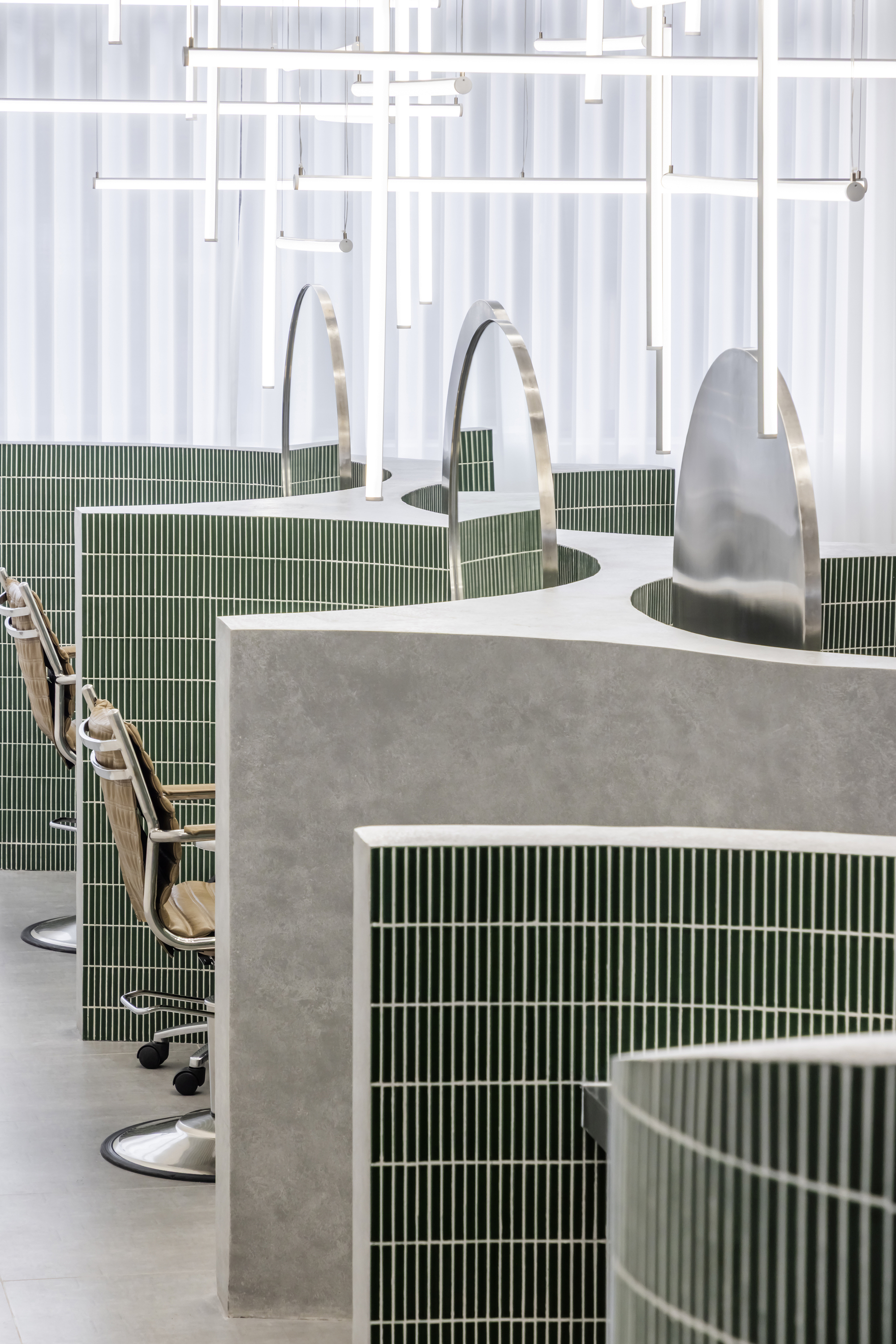 Salon stations with curved concrete and green tile bases beneath white translucent curtain dividers