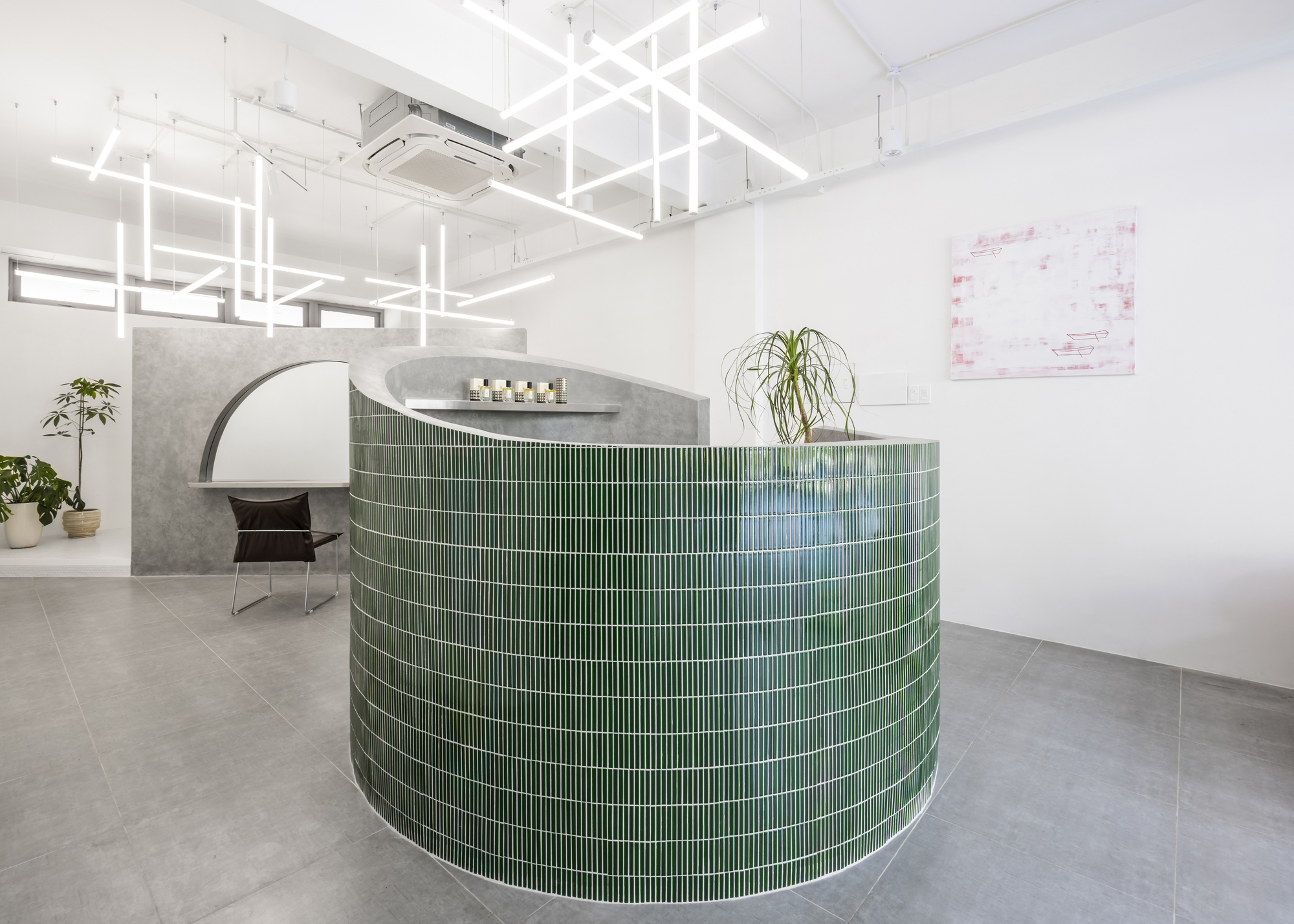Curved reception desk clad in green horizontal tile with potted plant and grid lighting overhead