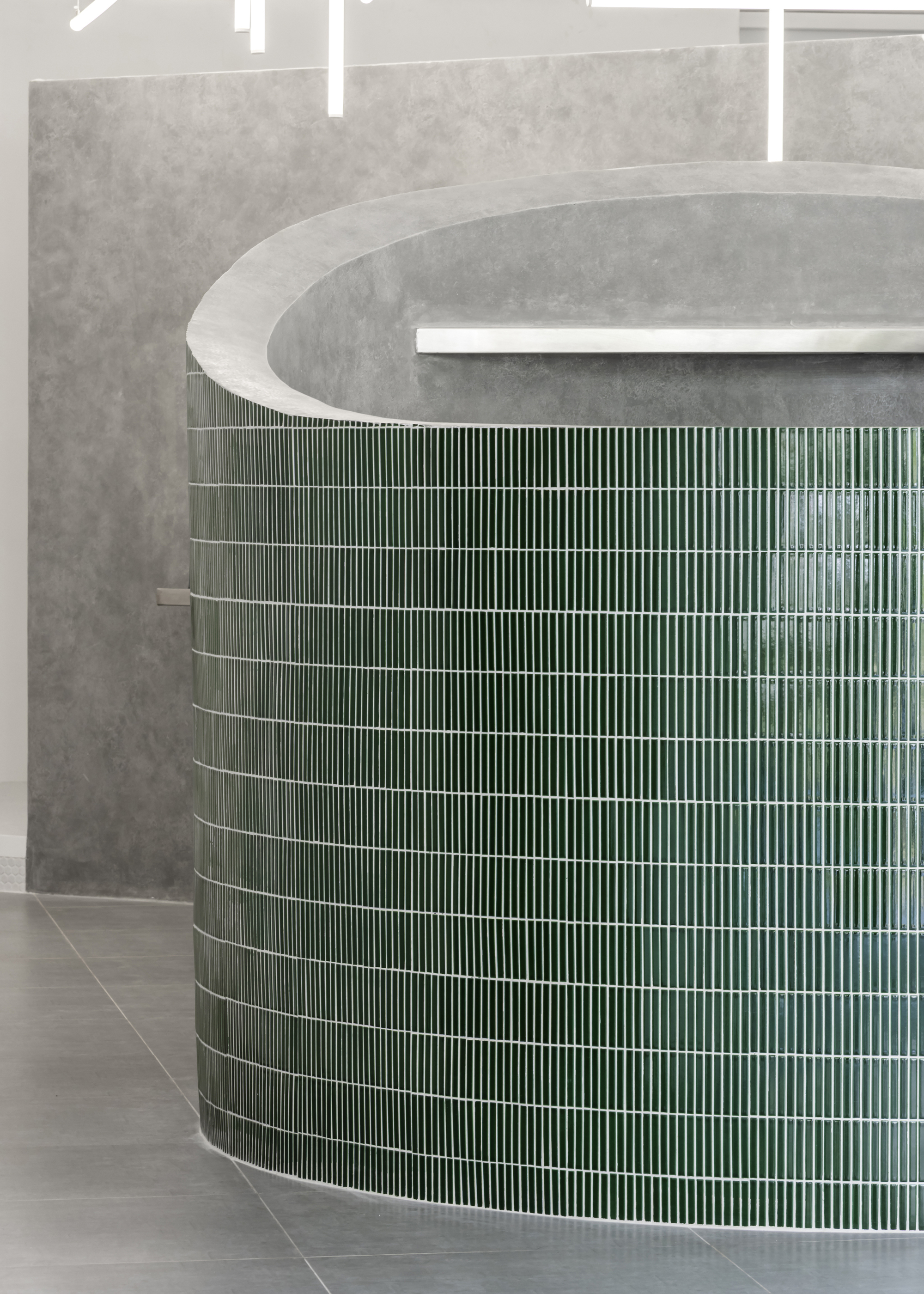 Curved counter clad in vertical green ceramic tiles beneath a concrete soffit