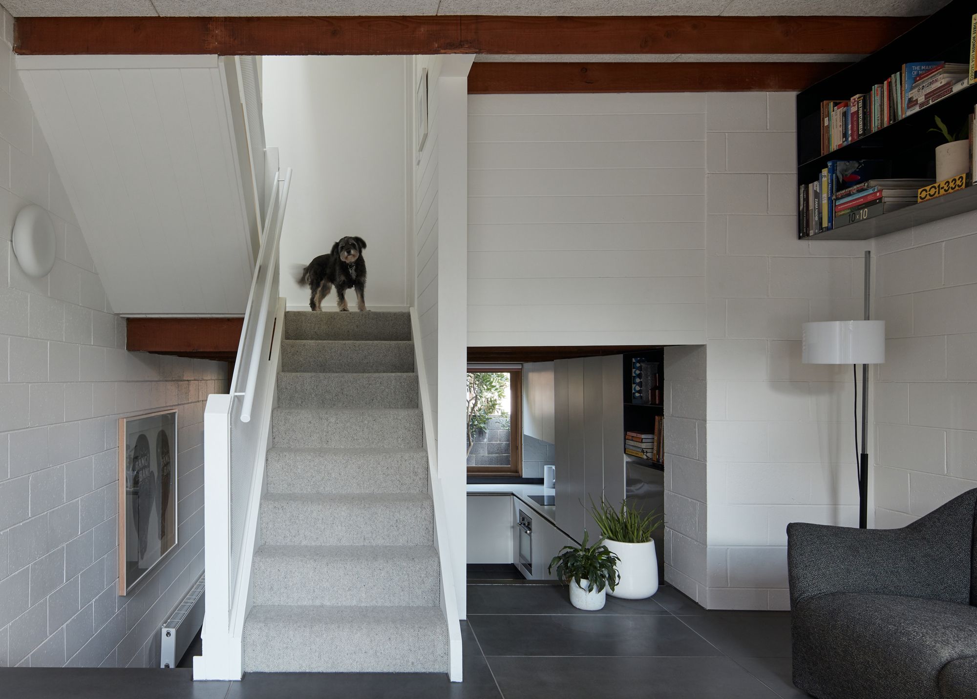 Interior staircase with grey tile walls, exposed timber beams, and a dog standing on the landing