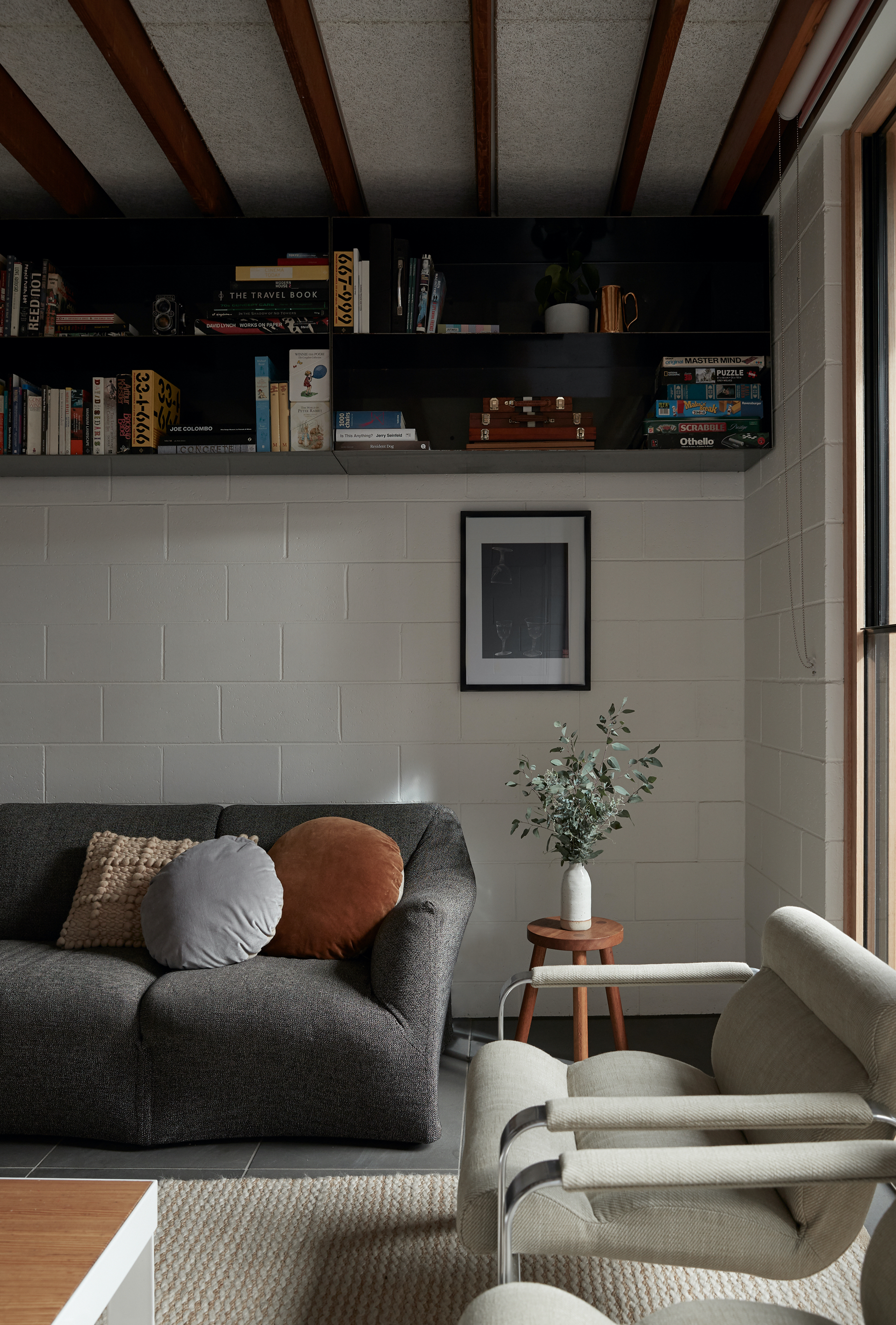 Living room with exposed timber ceiling beams and white brick wall below open bookshelves