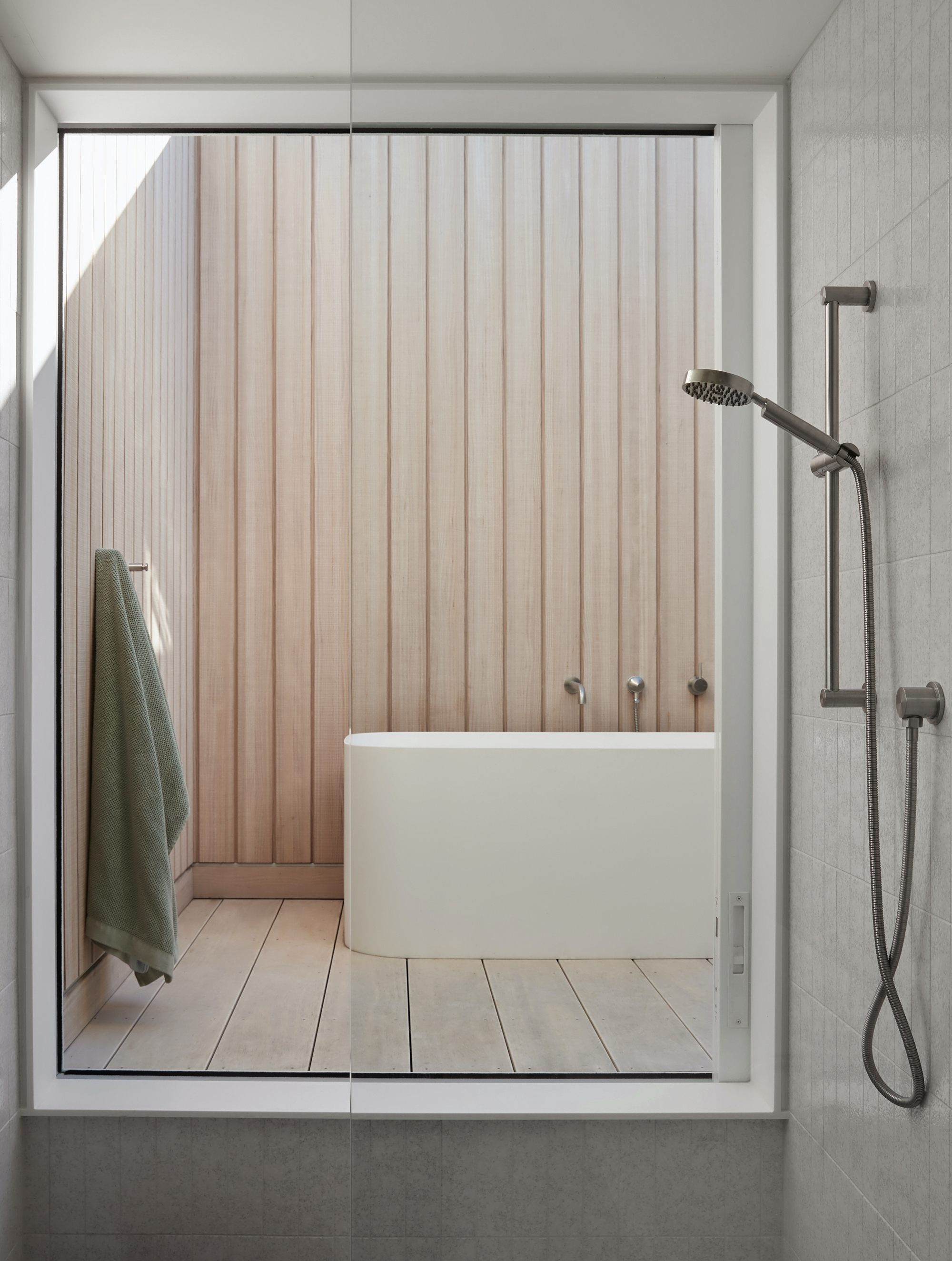 Glass shower enclosure framing view of freestanding tub against vertical timber slat wall