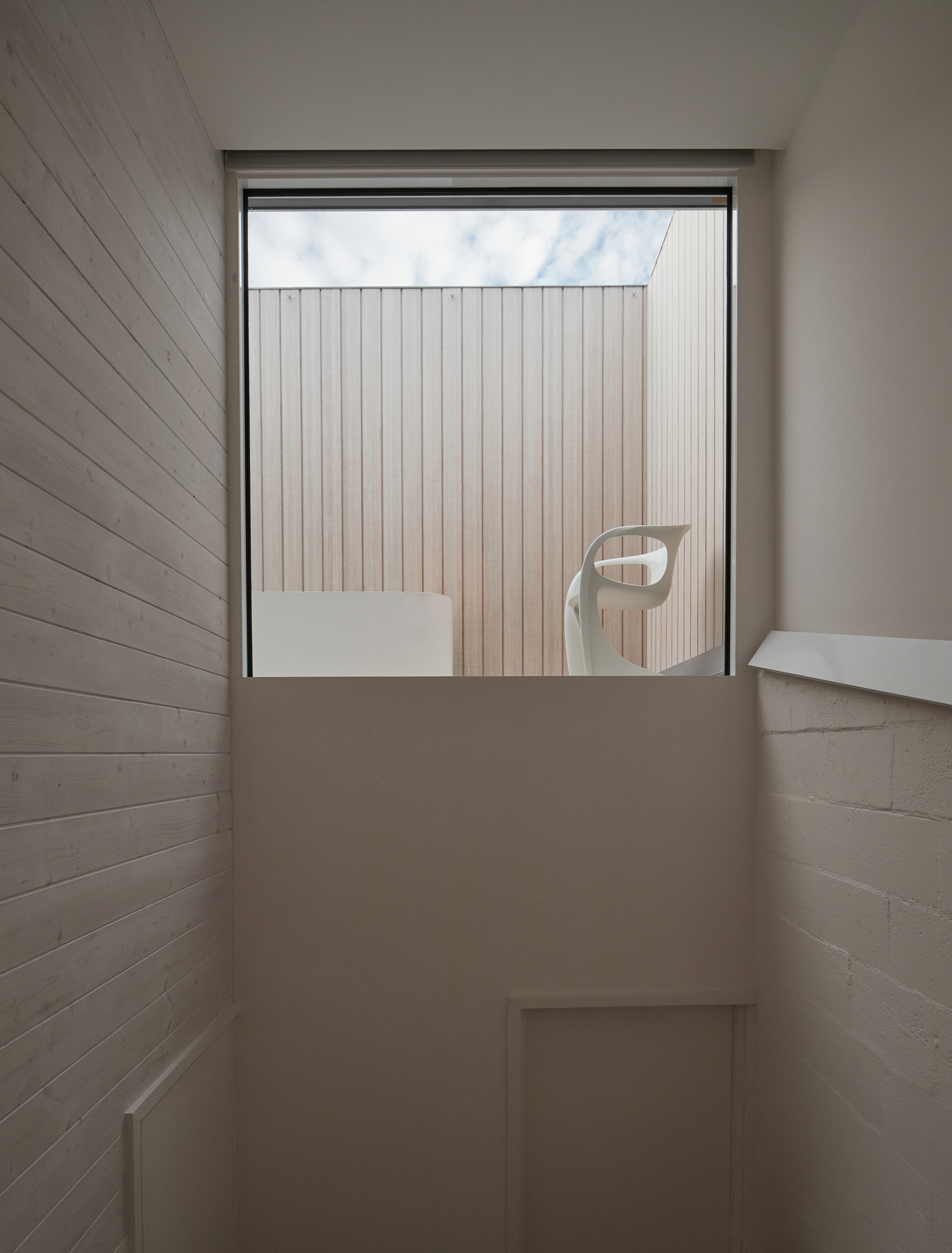 Window framing view of vertical timber cladding with chair reflection in glass