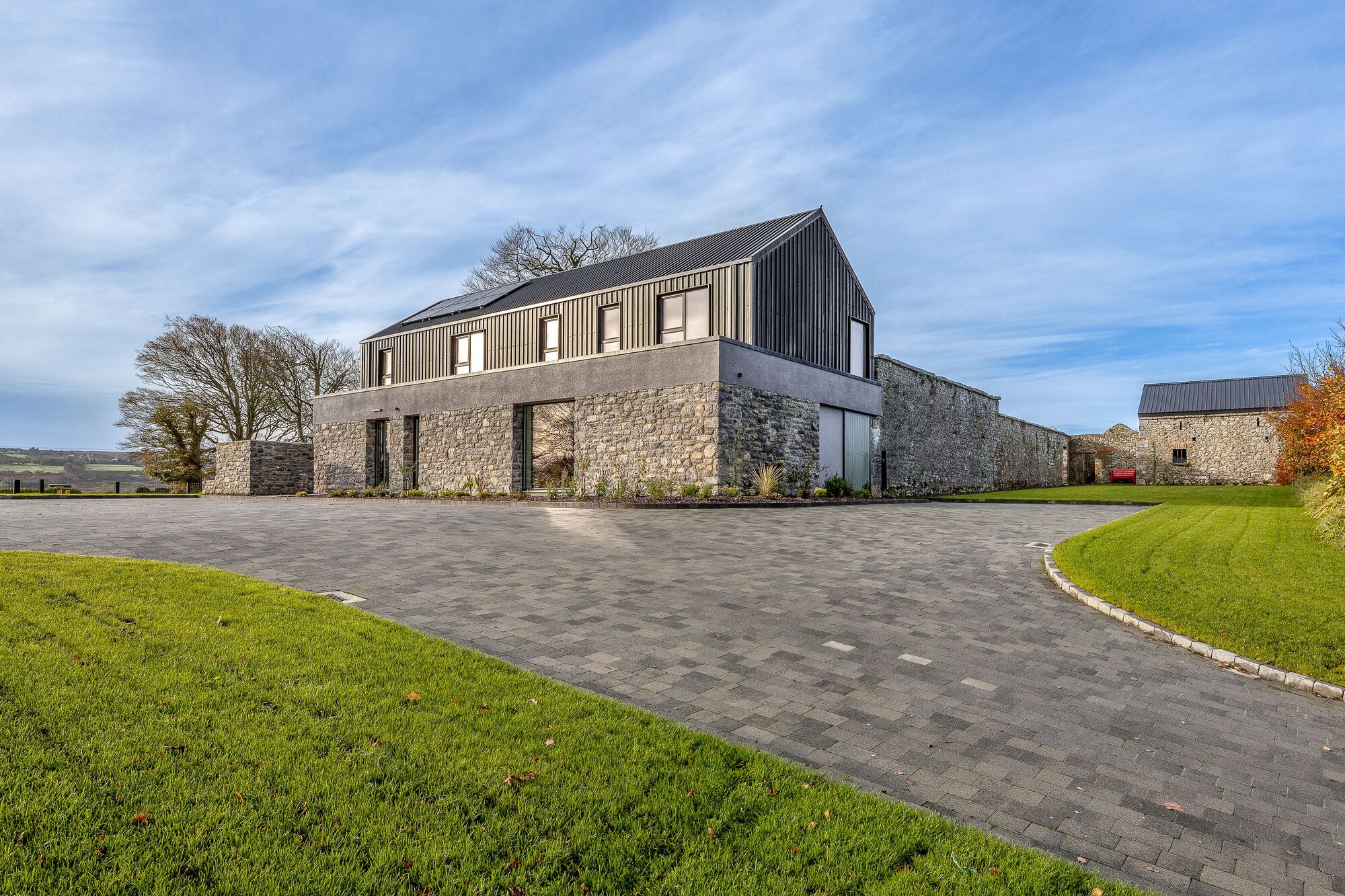 Stone base with corrugated metal upper volume viewed across a paved driveway and lawn