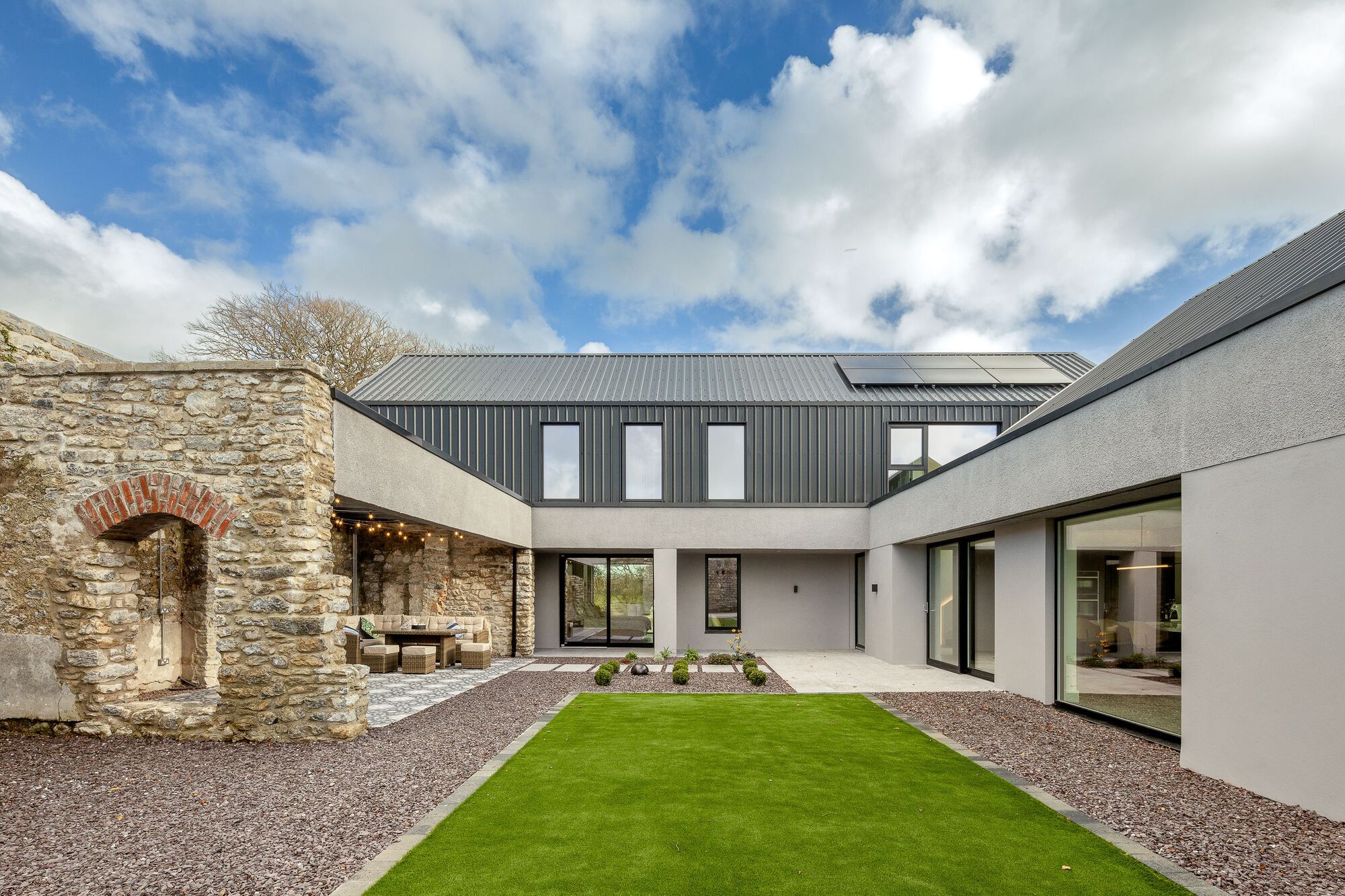 Internal courtyard with stone arch remnant and linked volumes under dramatic clouded sky