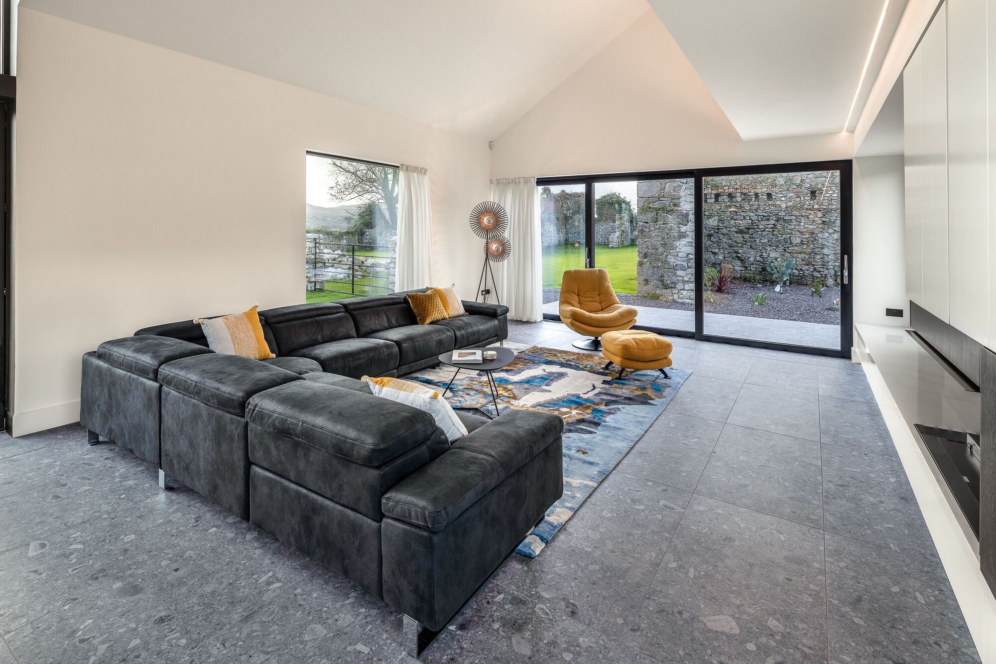 Living room with black modular sofa and floor-to-ceiling glazing overlooking a stone wall