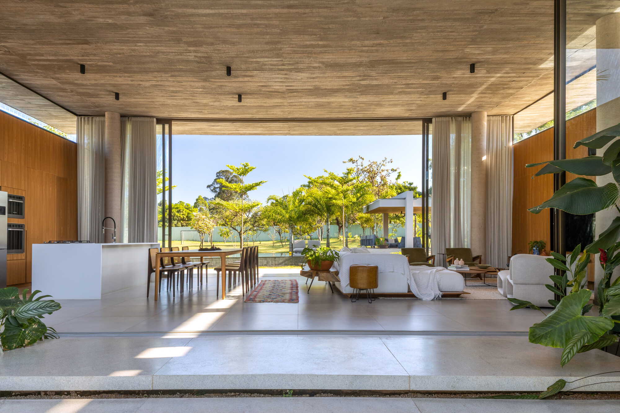 Open-plan living space with timber ceiling and retractable curtains opening to the pool terrace